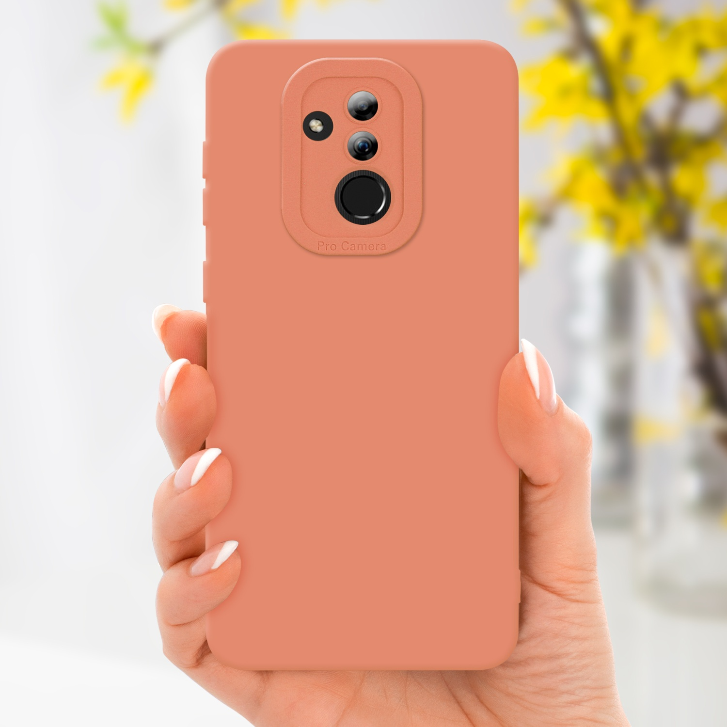 Una mano che tiene una custodia color pesca per telefono con fotocamera pro. Fiori gialli sullo sfondo.