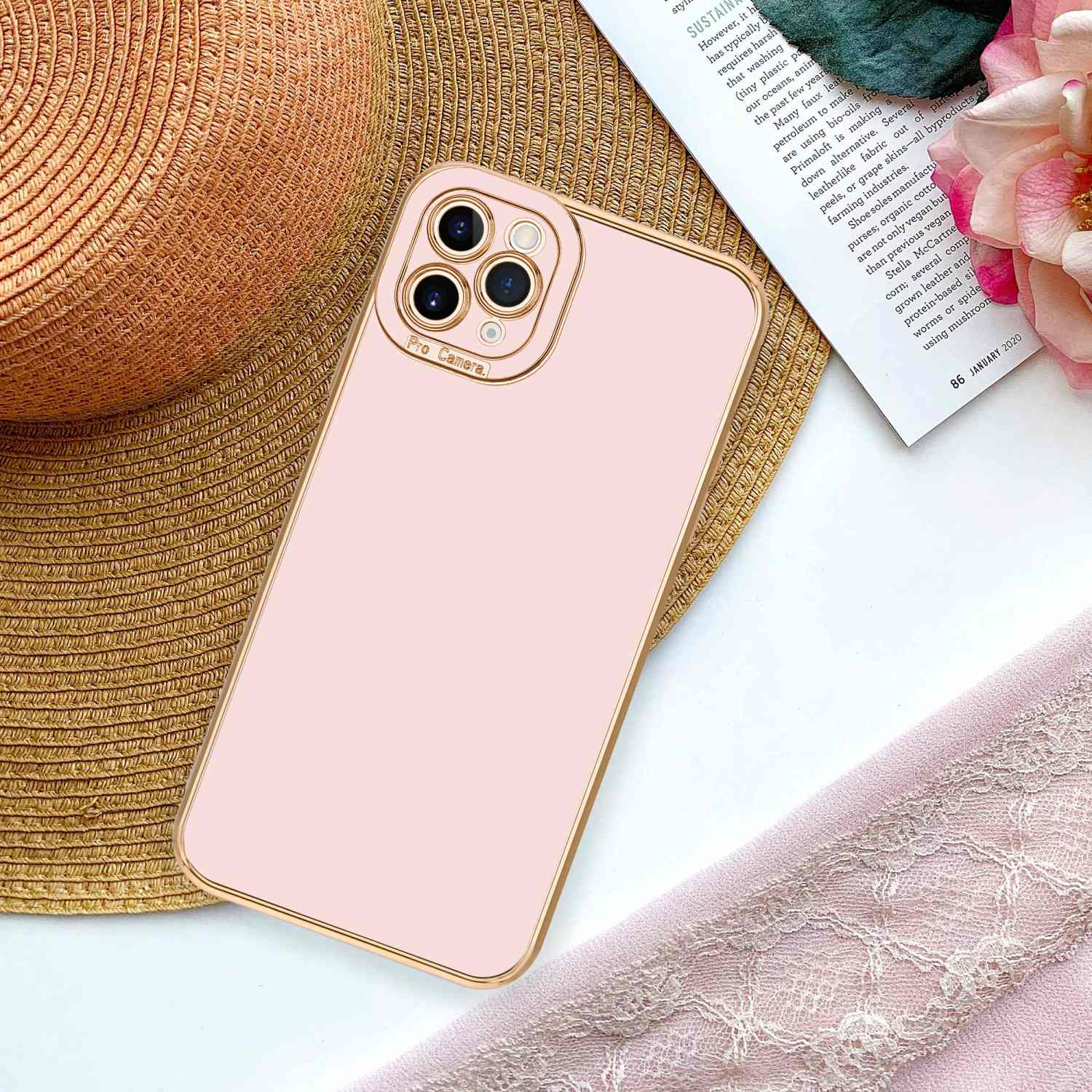 Ein Telefon mit rosafarbenem Gehäuse und goldenem Rahmen liegt neben einer Zeitschrift und einer Blume.