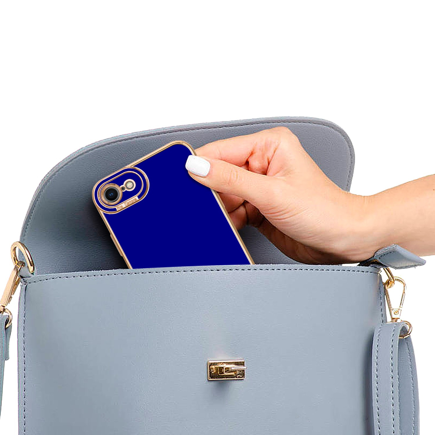 Hand legt eine dunkelblaue Handyhülle in eine graue Handtasche. Die Tasche hat einen goldenen Rahmen.