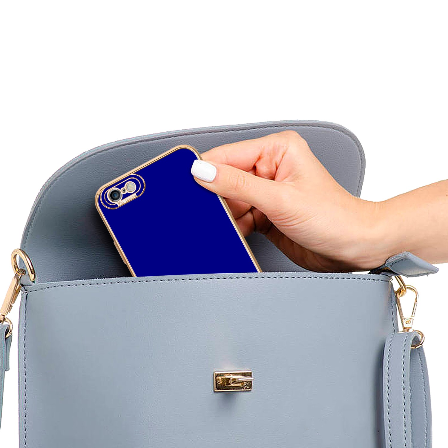 Hand legt blaues Telefon in blaue Handtasche. Goldakzente auf Tasche und Handyhülle.