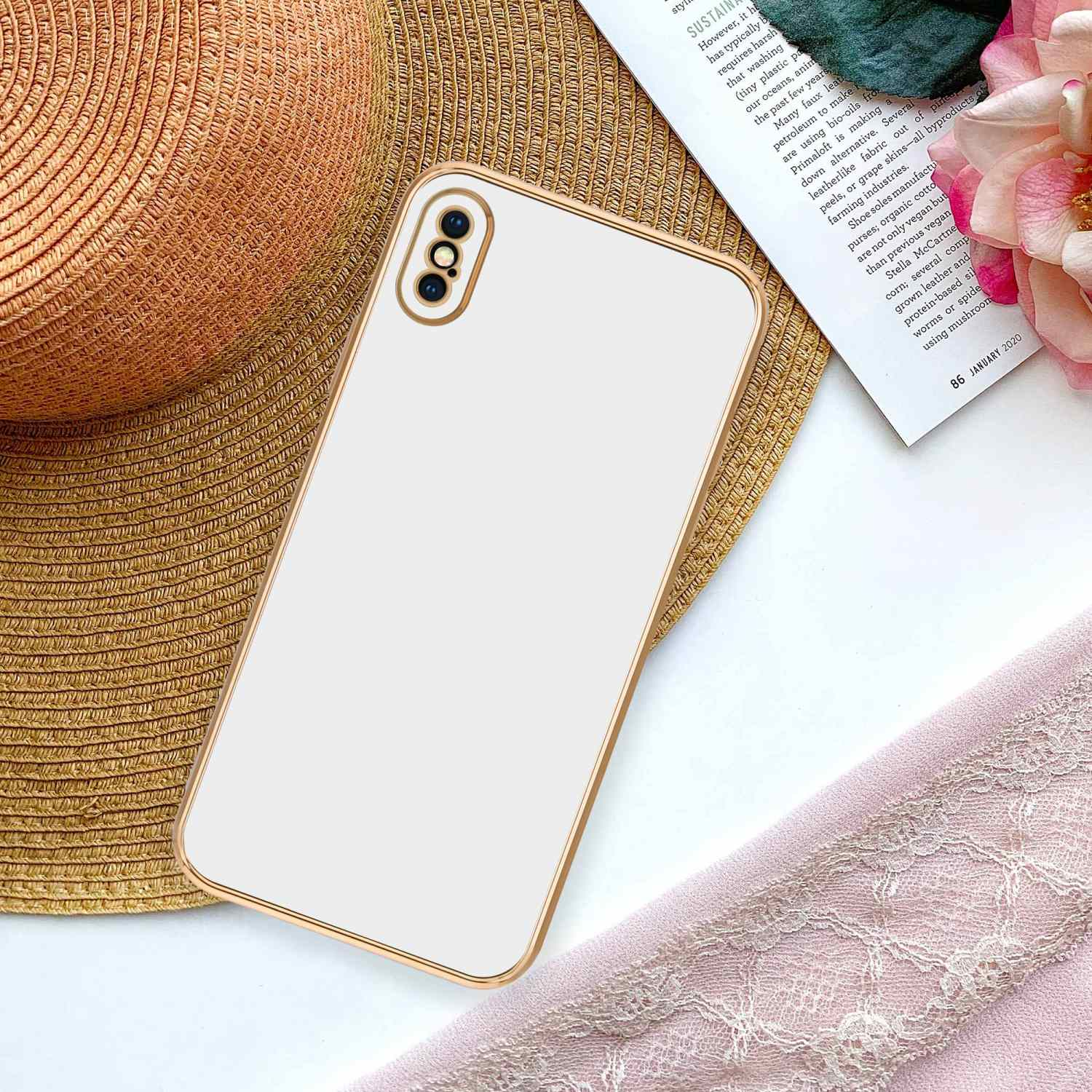 Weißes Telefon mit goldfarbenem Gehäuse. Das Telefon liegt auf einer Zeitschrift neben einer rosa Blume.