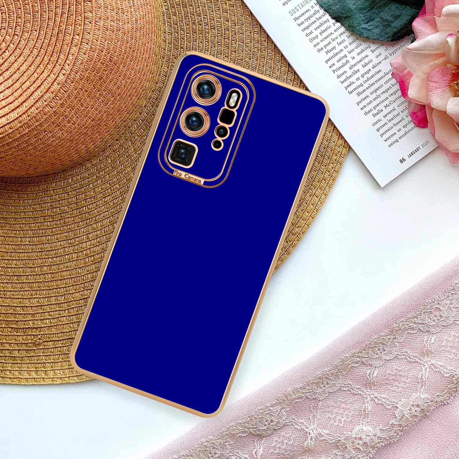 Eine blaue Handyhülle auf einem Tisch mit Zeitschrift und Hut. Die Hülle hat einen goldenen Rahmen und Kameradetails.