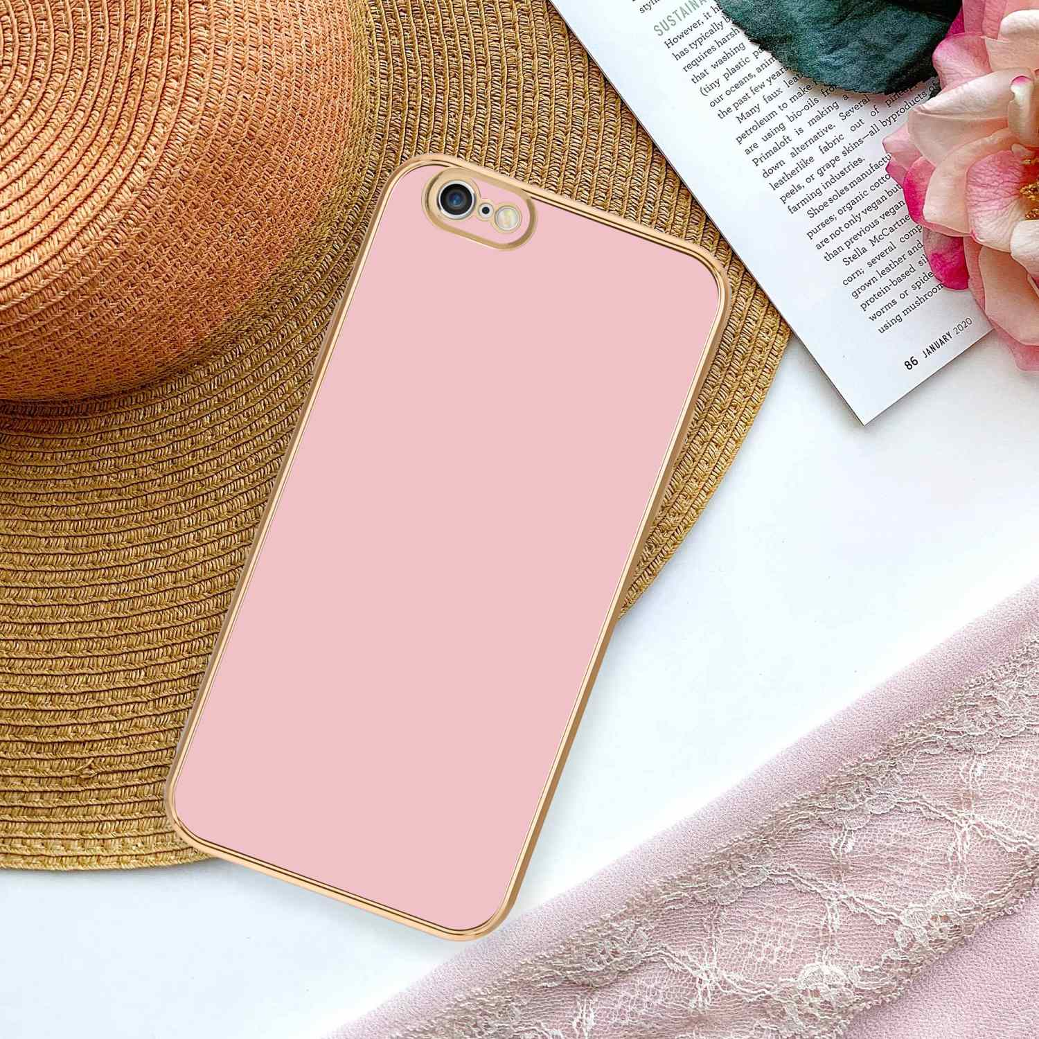 Rosa Handyhülle auf einem Telefon, neben Hut, rosa Stoff und Zeitschrift.