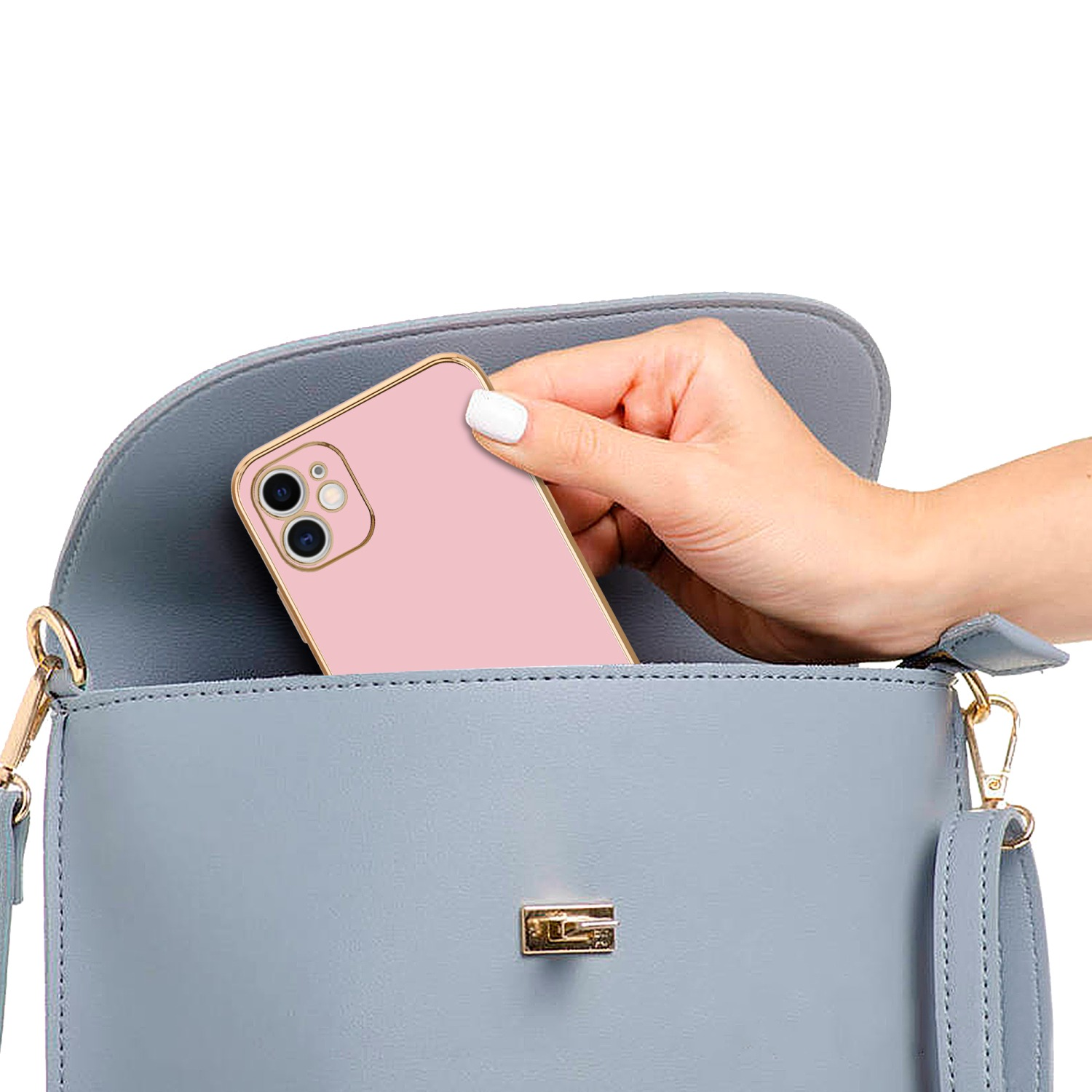 Hand legt eine rosa Handyhülle in eine graue Handtasche. Die Tasche hat einen goldenen Rahmen.