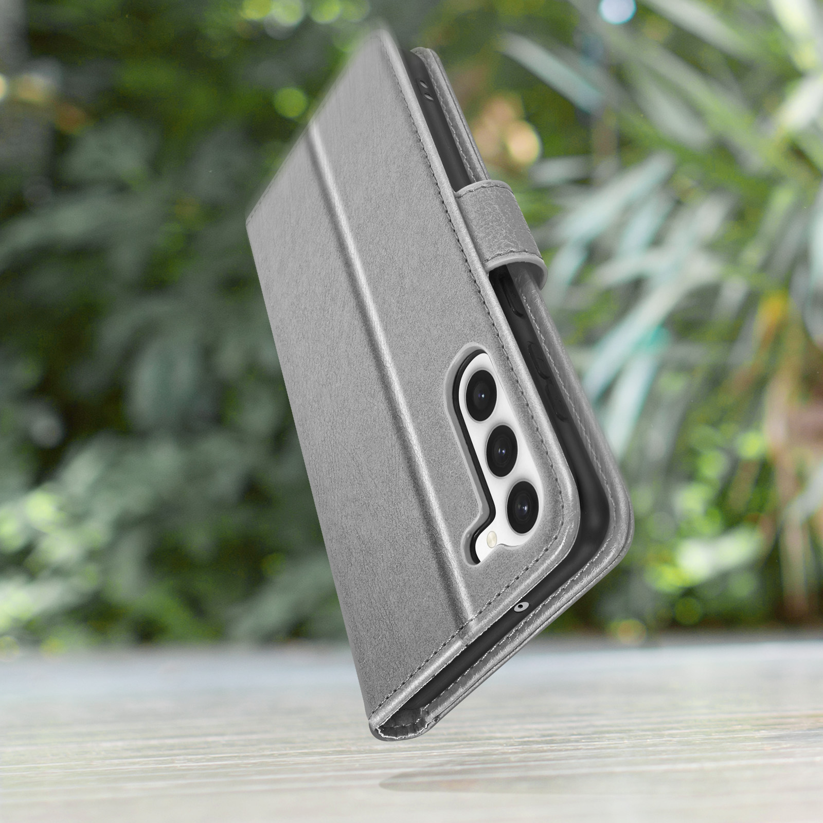 Graue Handyhülle in Buchform, mit einem Telefon im Vordergrund mit grünem Hintergrund.