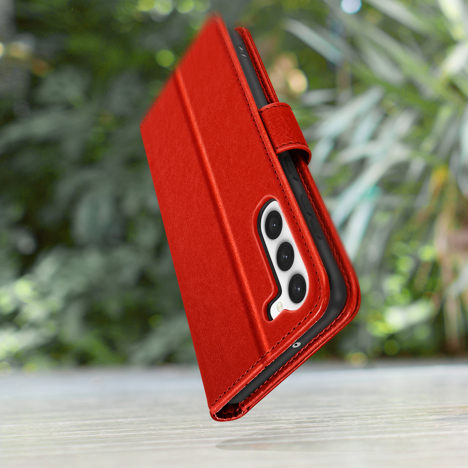 Rode telefoonhoes met flap, buiten. De hoes ligt op een houten oppervlak met een wazige groene achtergrond.