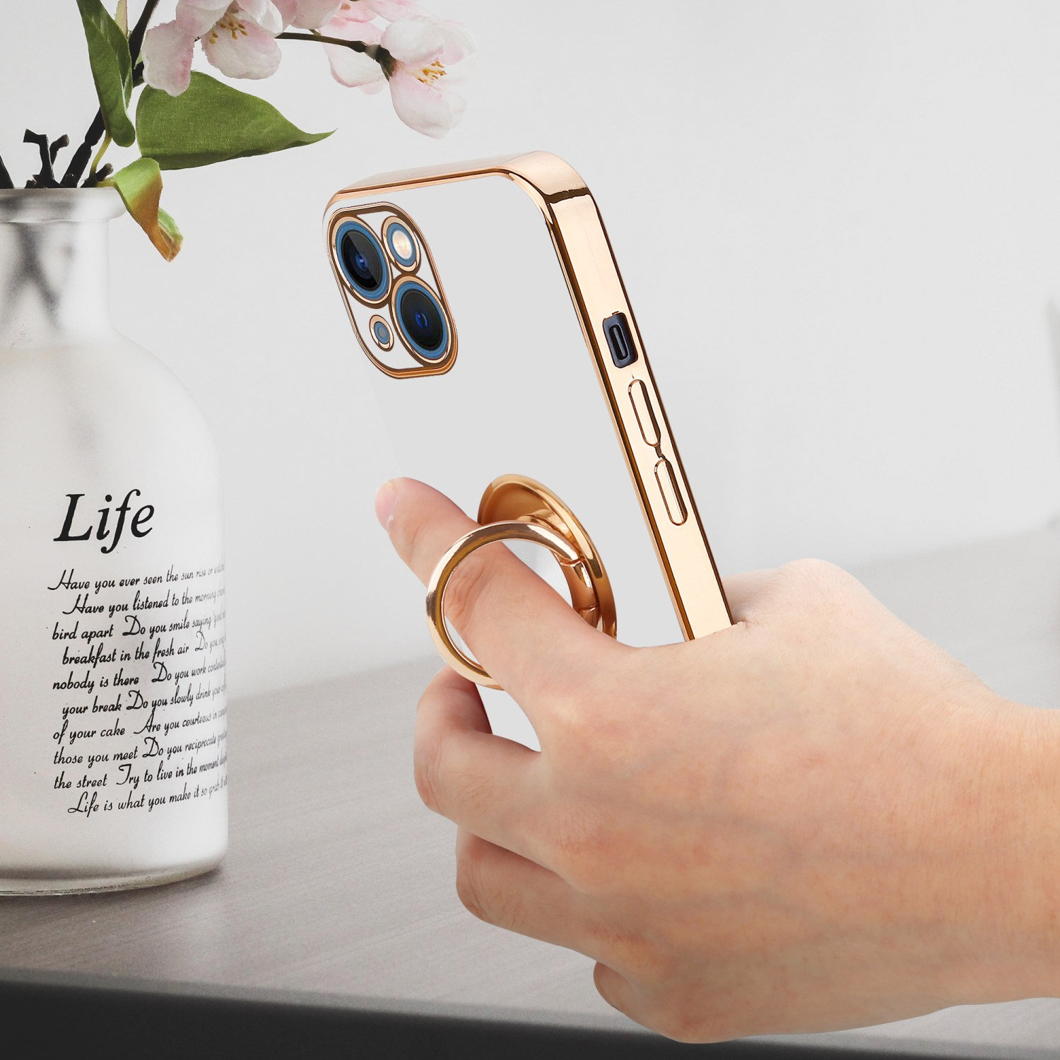Eine Hand hält ein Telefon mit Ringhalter. Im Hintergrund eine Vase.