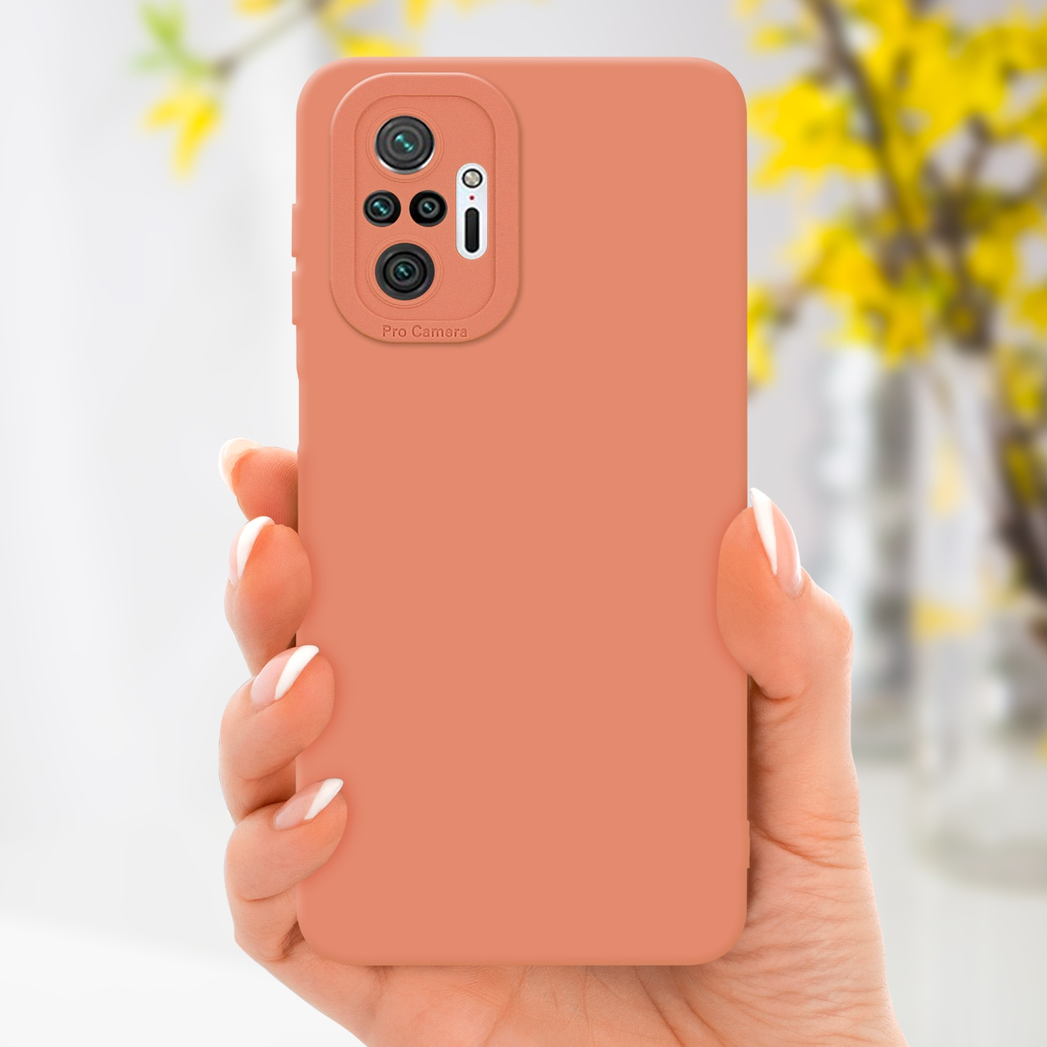 Eine Hand, die eine orangefarbene Handyhülle mit einer Profi-Kamera hält. Gelbe Blumen im Hintergrund.