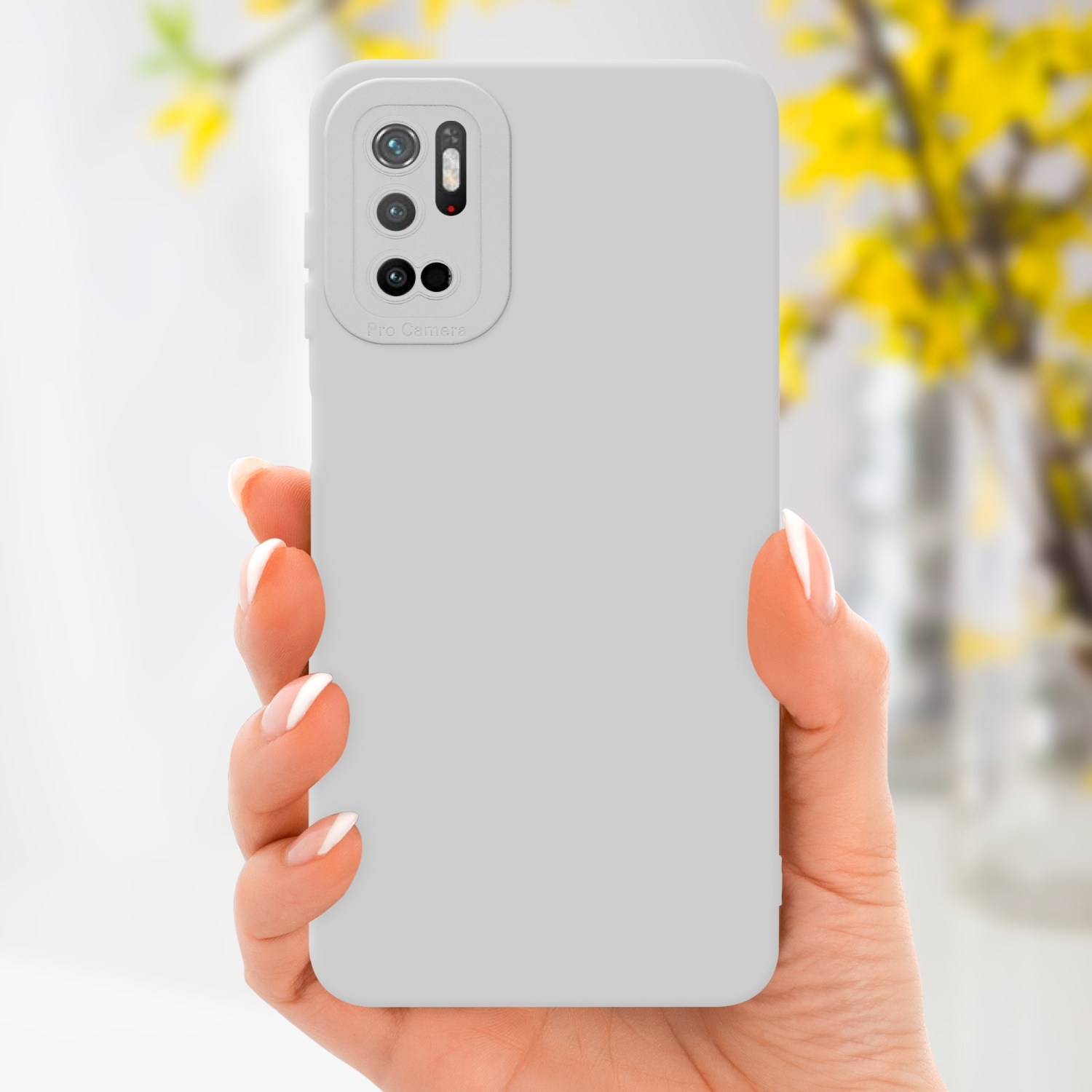 Mano che tiene una custodia per telefono grigio chiaro. Fiori gialli in un vaso sullo sfondo. Sfondo bianco.