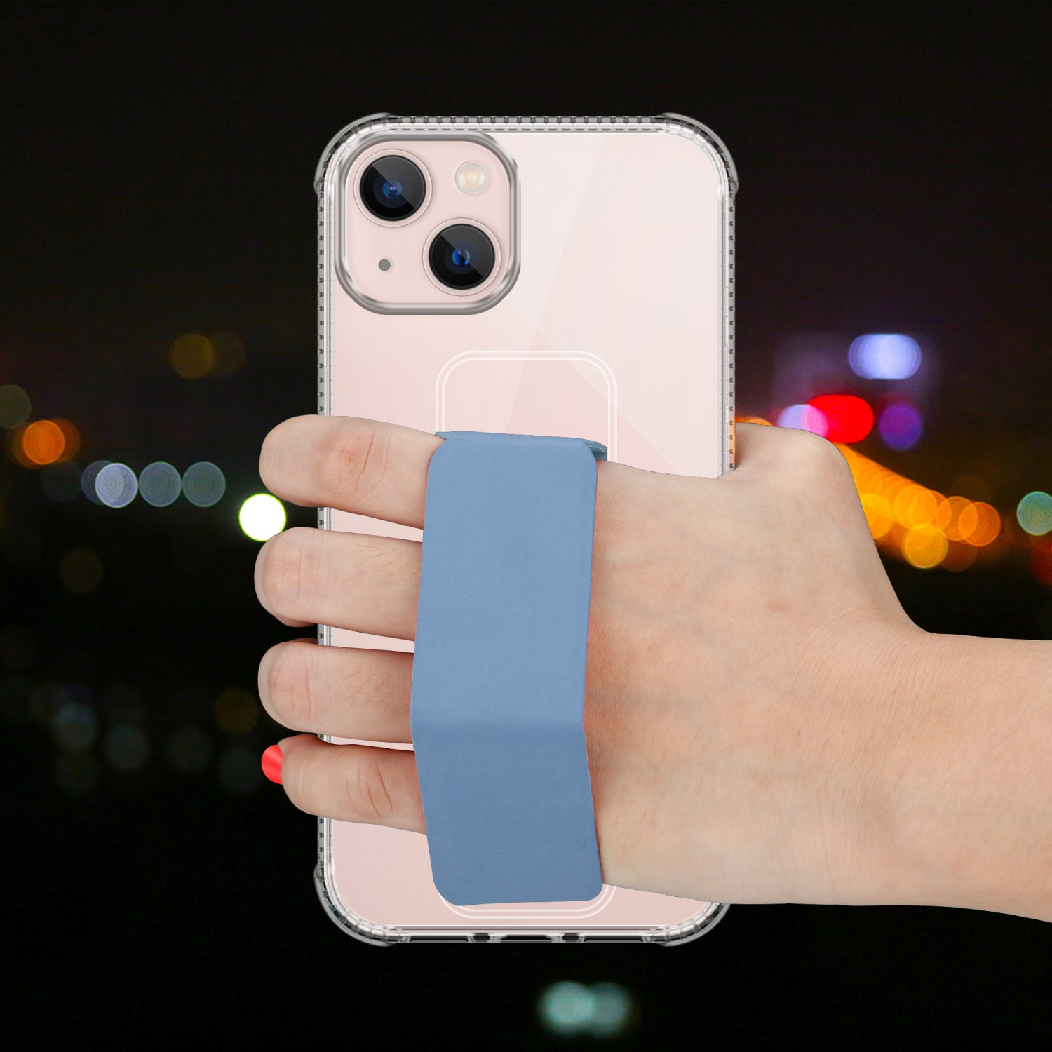 Hand hält klares Telefon mit blauem Riemen, vor verschwommenem Nachthintergrund.