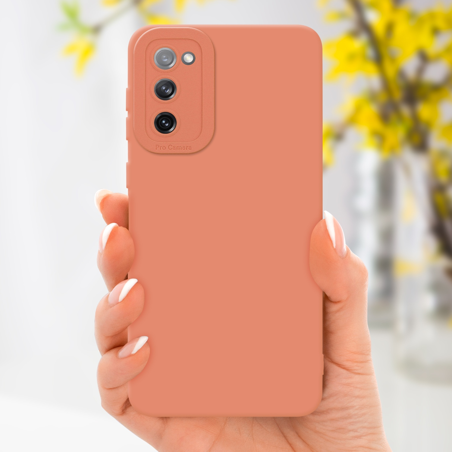 Mano che tiene una custodia per telefono color pesca. Sfondo con fiori gialli.
