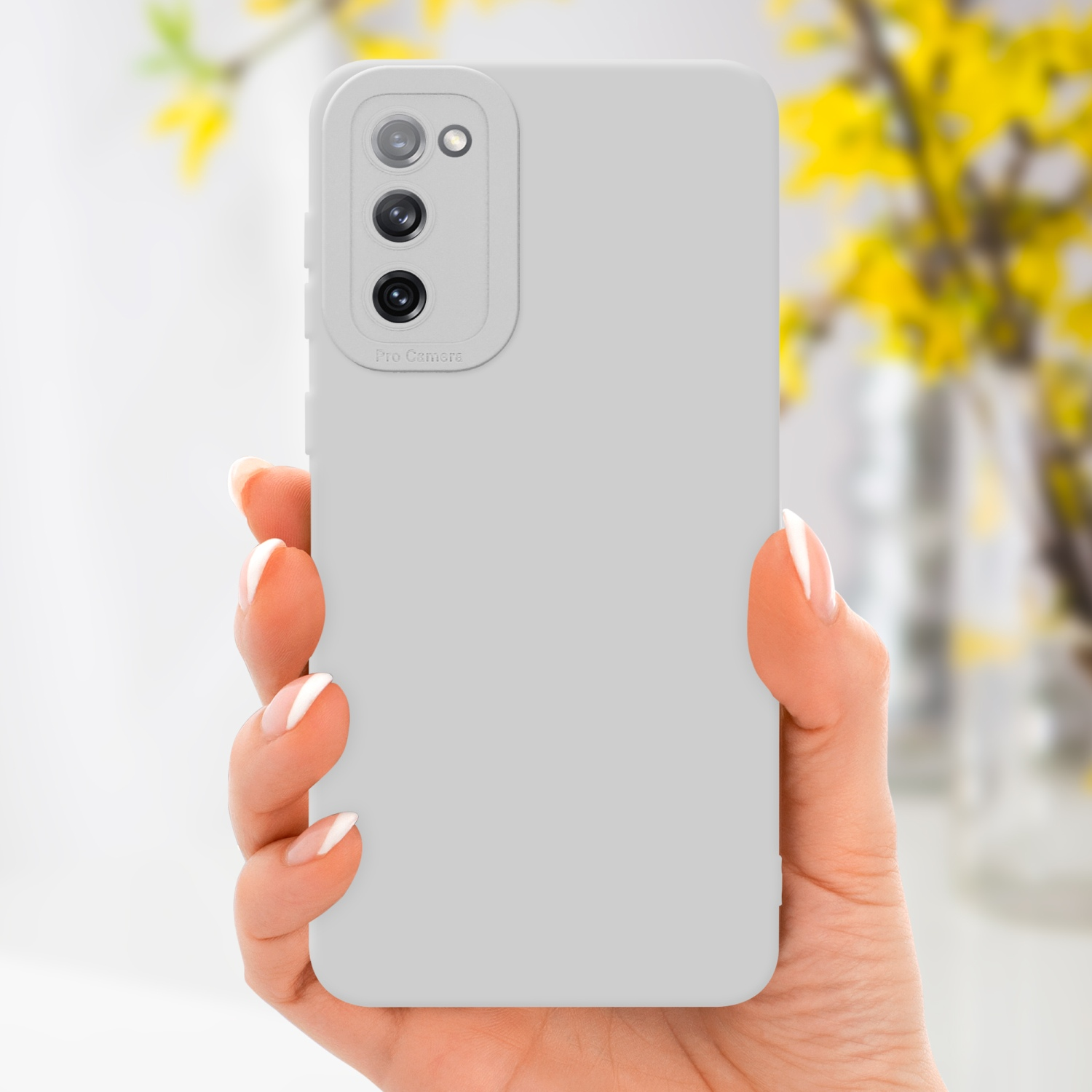 Una mano che tiene una custodia grigia per telefono con un'etichetta pro camera e uno sfondo floreale sfocato.