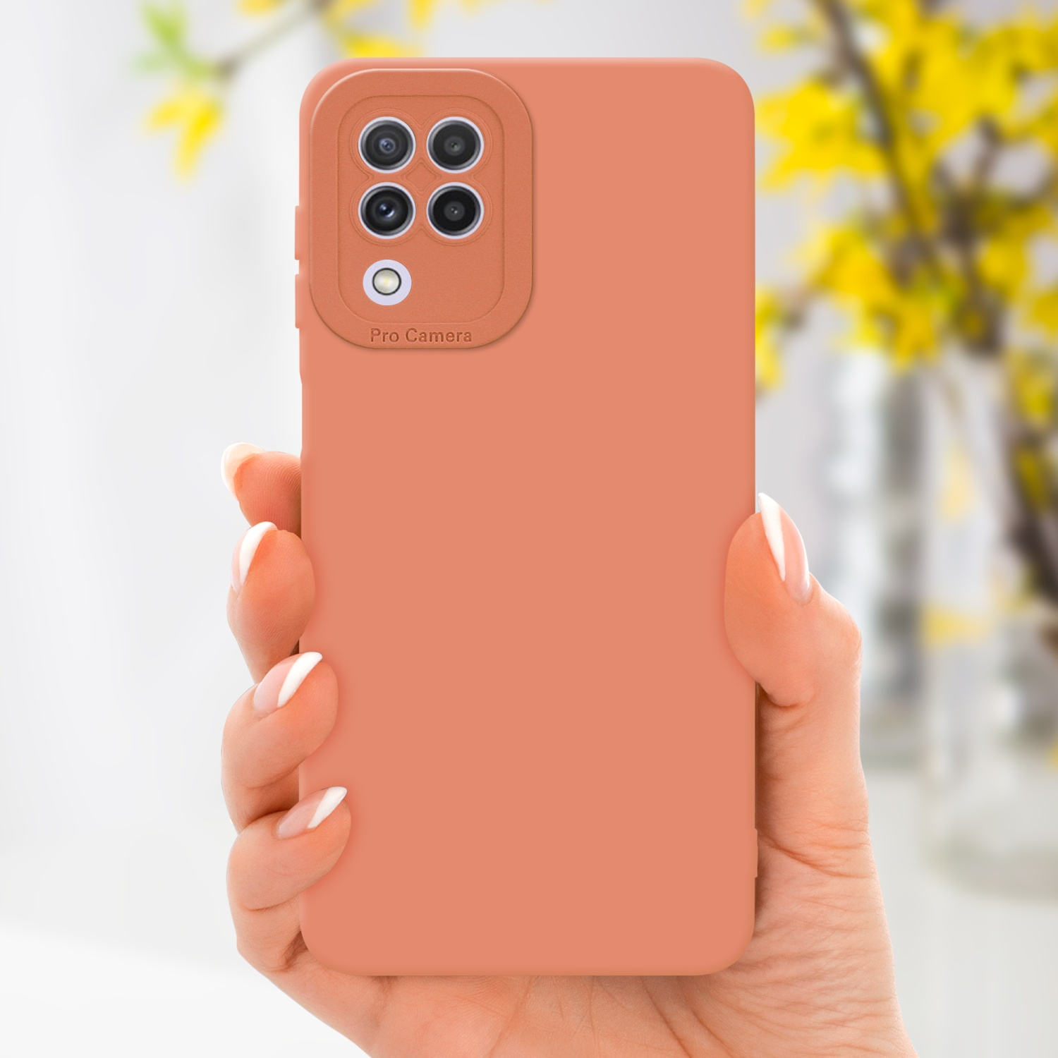 Une main tenant une coque de téléphone pêche. Des fleurs jaunes sont floues en arrière-plan.