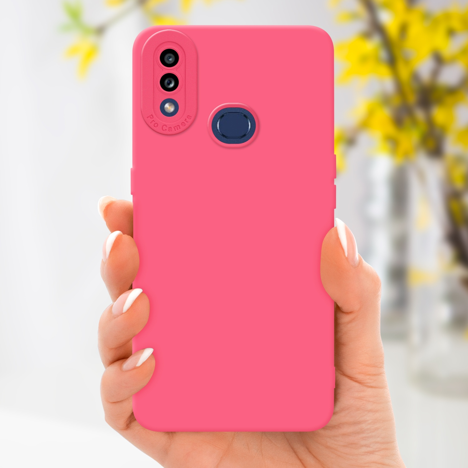 Una mano tiene una custodia rosa per telefono, con sezione fotocamera. Fiori gialli sullo sfondo.