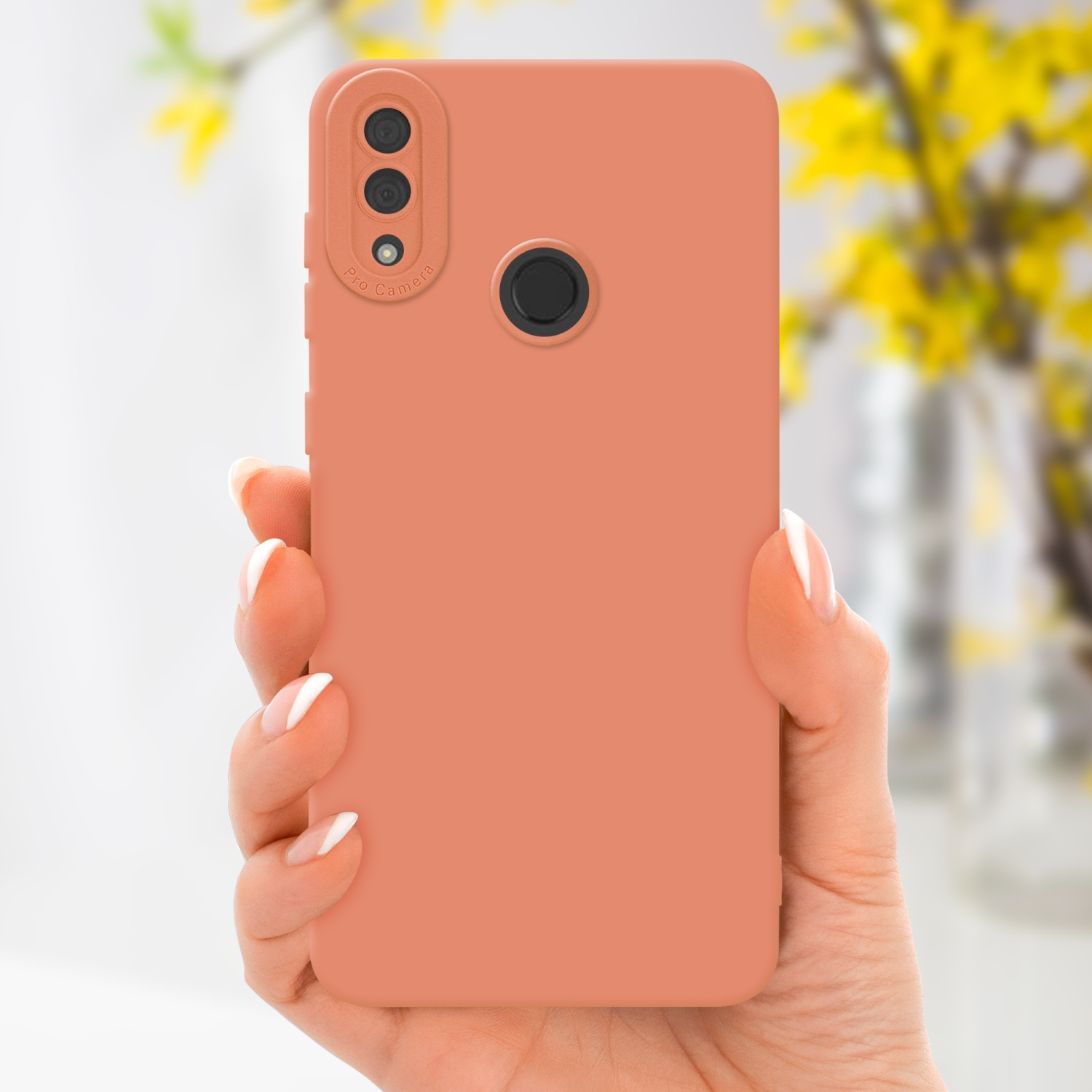 Una mano che tiene una custodia color pesca per telefono con un'etichetta pro camera e uno sfondo floreale sfocato.