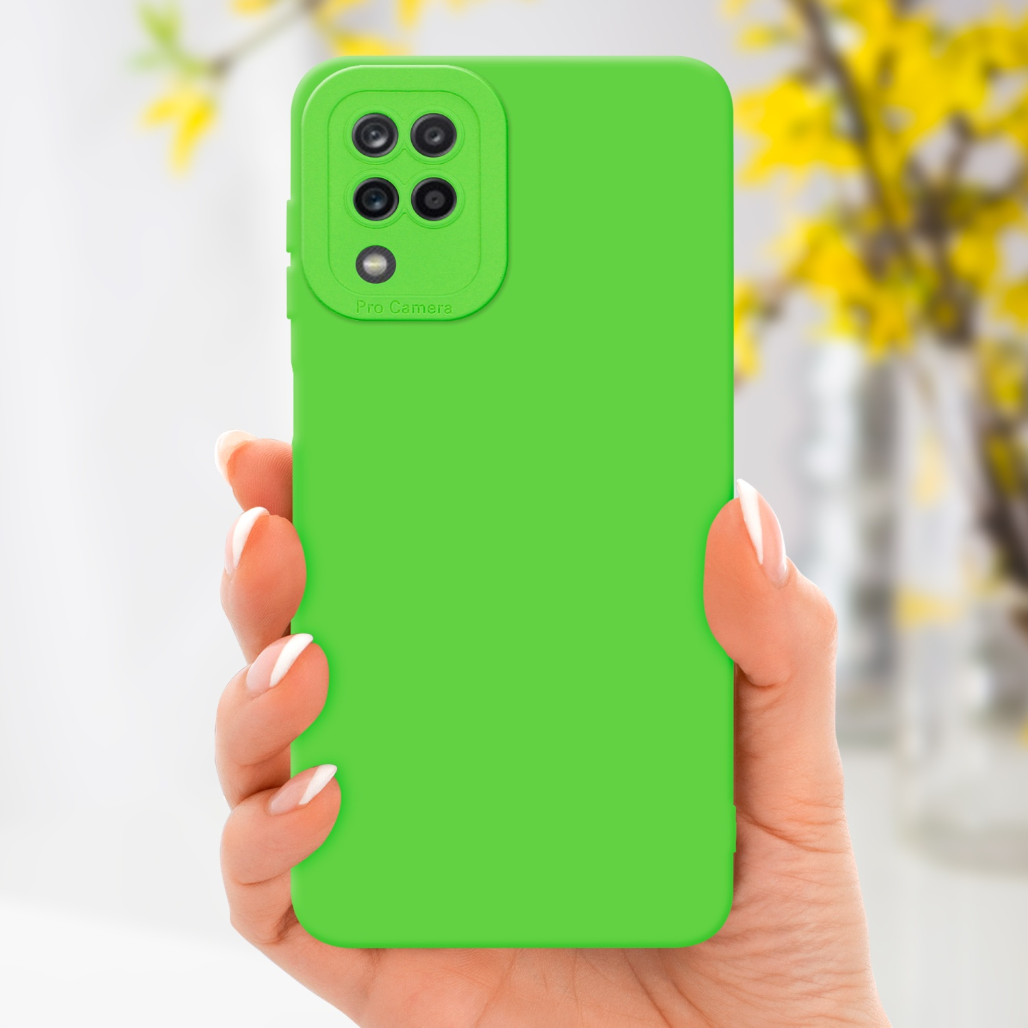 Una mano tiene un telefono verde con una custodia verde. Fiori gialli sfocati sullo sfondo.