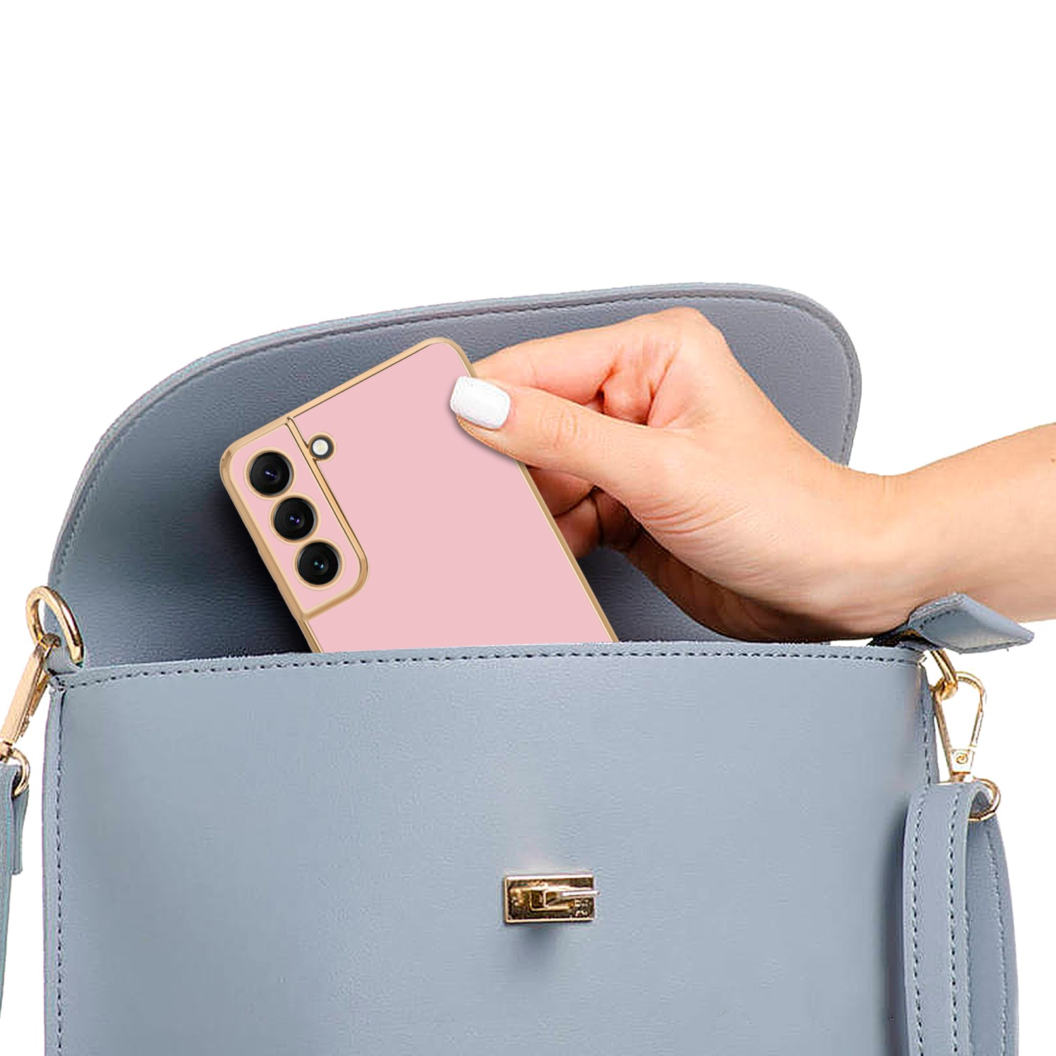 Hand legt ein pinkes Telefon in eine hellblaue Handtasche mit goldfarbenem Verschluss.