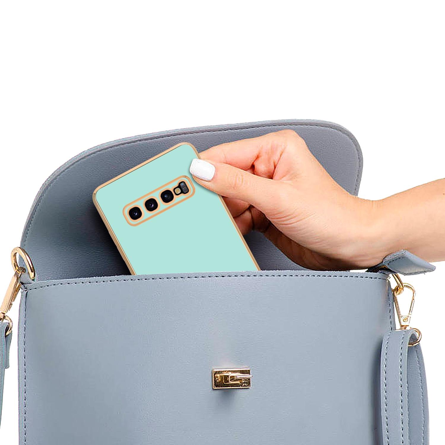 Eine Hand legt ein mintfarbenes Telefon in eine blaue Handtasche. Das Telefon hat einen goldenen Rand.
