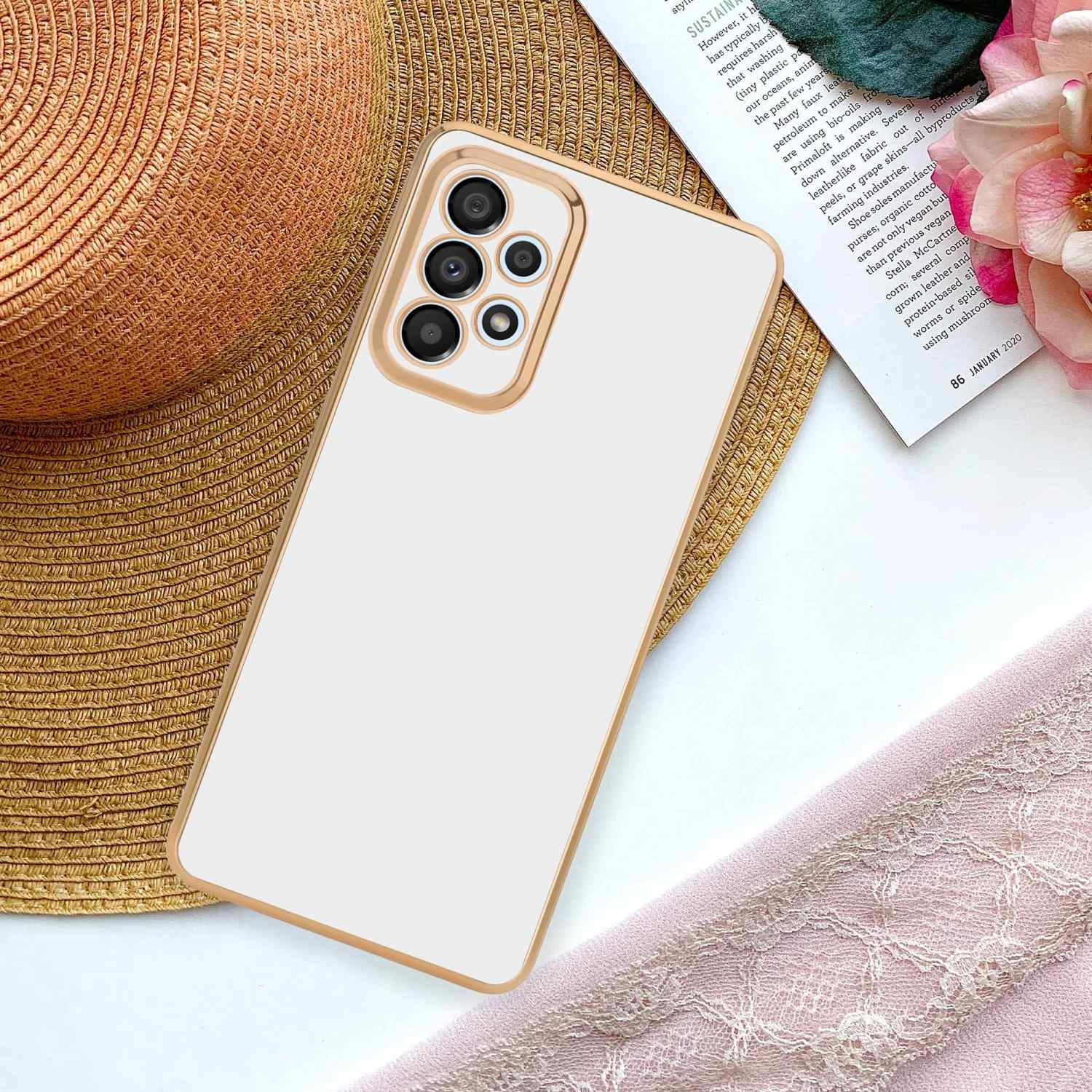 Weißes Telefon mit goldenem Rahmen auf dem Tisch. Der Hintergrund ist ein Magazin, Blumen und Stoff.