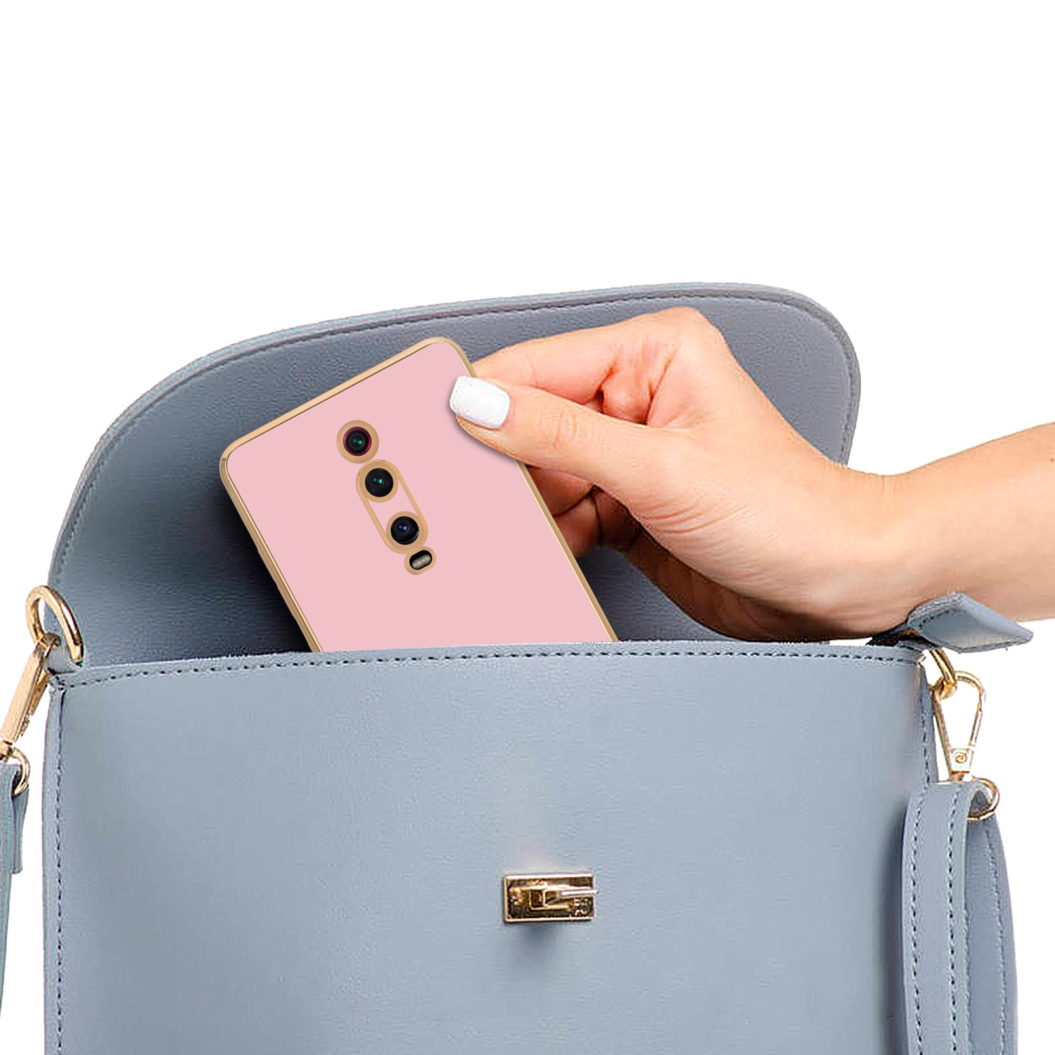 Hand legt rosa Telefon in graue Handtasche. Goldakzente sind sichtbar.