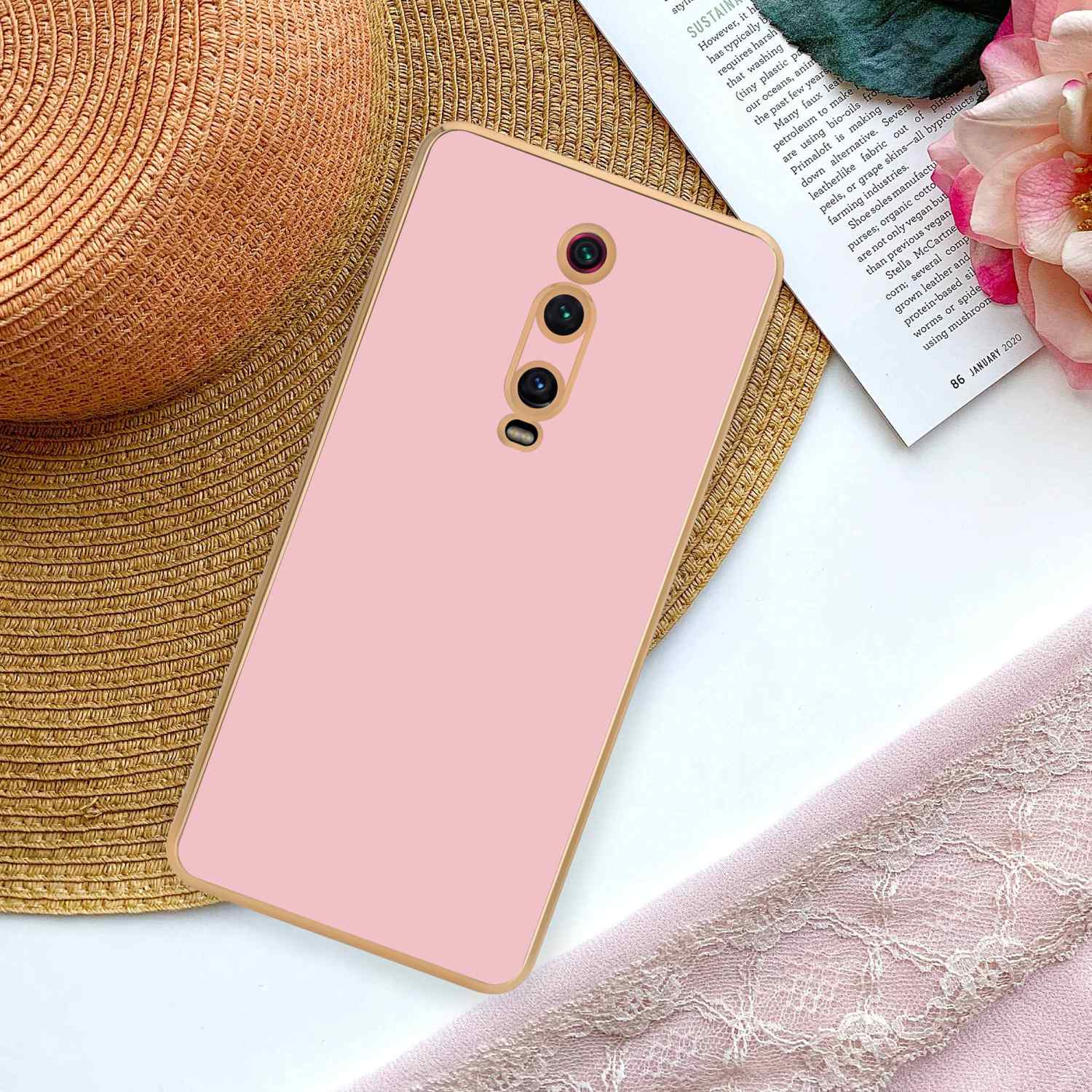 Eine pinkfarbene Handyhülle mit Goldkanten auf einem Tisch mit Magazin und rosa Stoff.