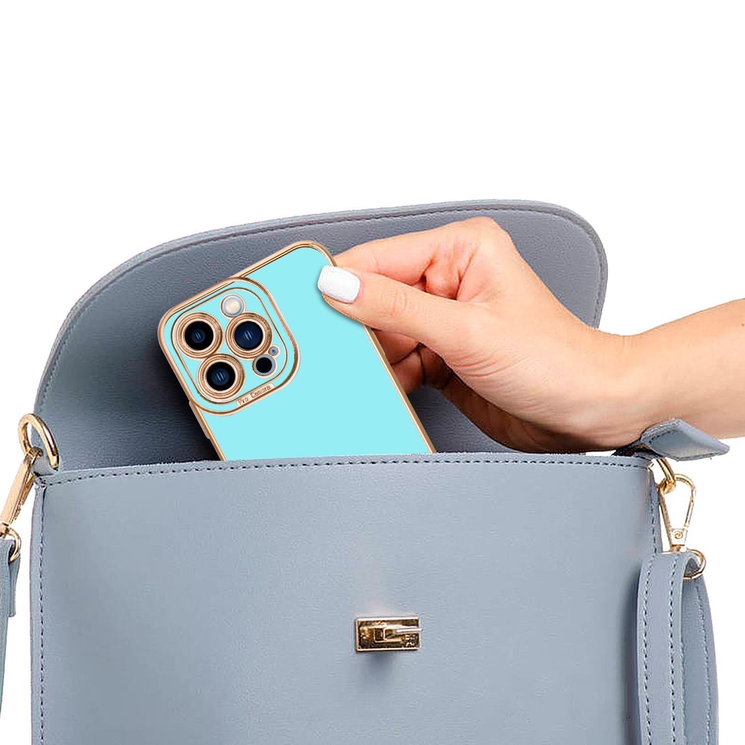 Eine Hand legt ein Telefon in eine Handtasche. Das Telefon ist blau mit goldenen Rändern.