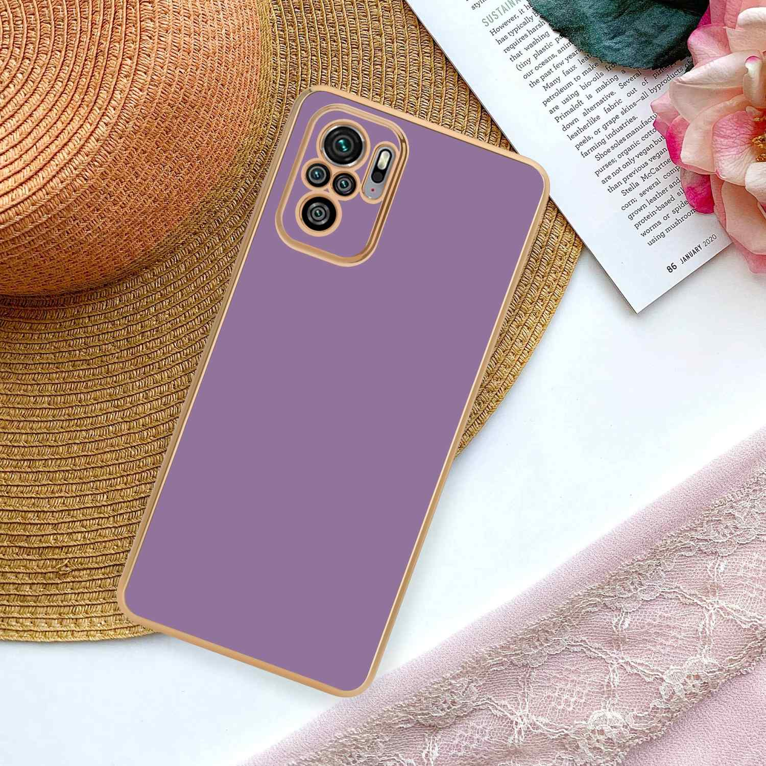 Custodia per telefono viola su un cappello di paglia intrecciata e una rivista. Nastro rosa e fiore sullo sfondo.