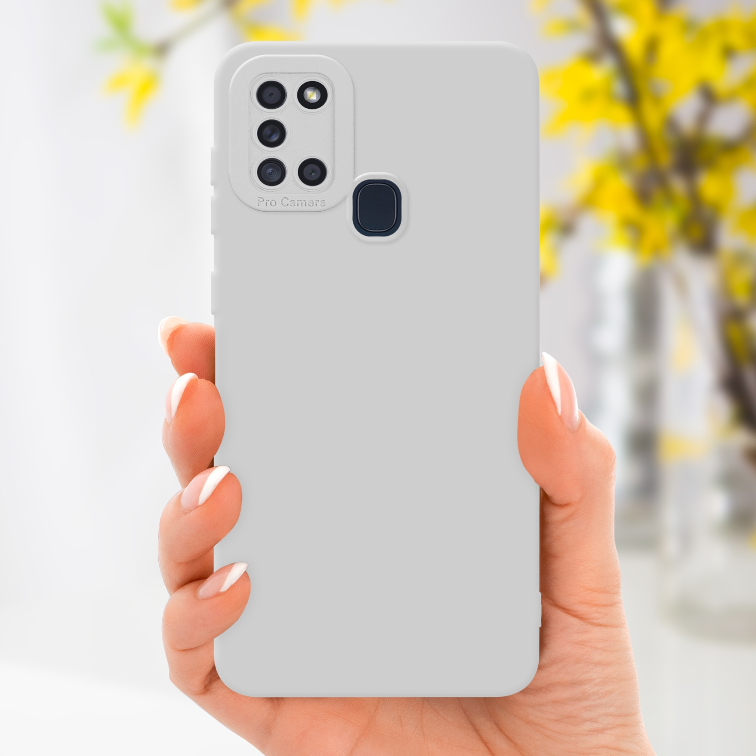 Una mano tiene una custodia grigia per telefono. Lo sfondo mostra un vaso sfocato di fiori gialli.