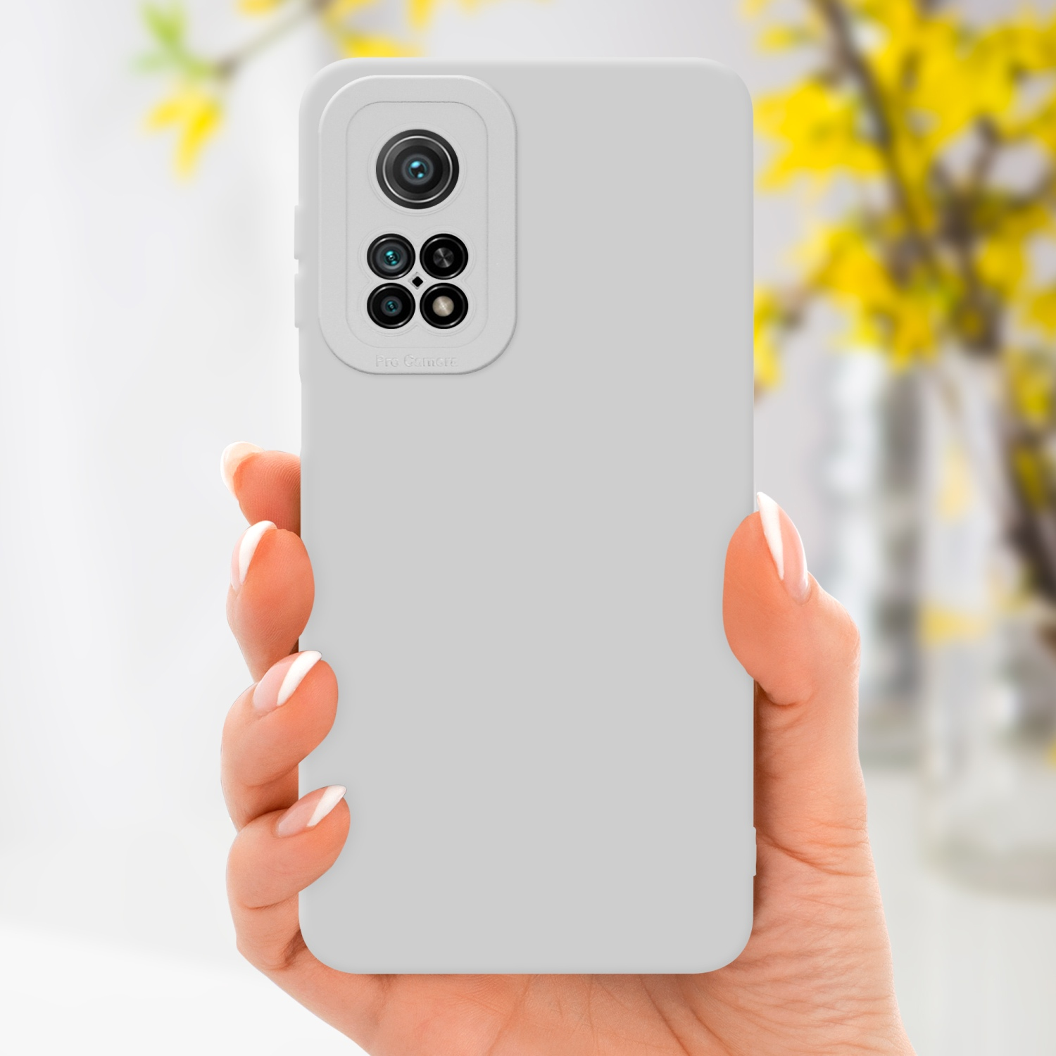 Mano che tiene una custodia per telefono grigio chiaro con un dosso per fotocamera. Fiori gialli sullo sfondo.