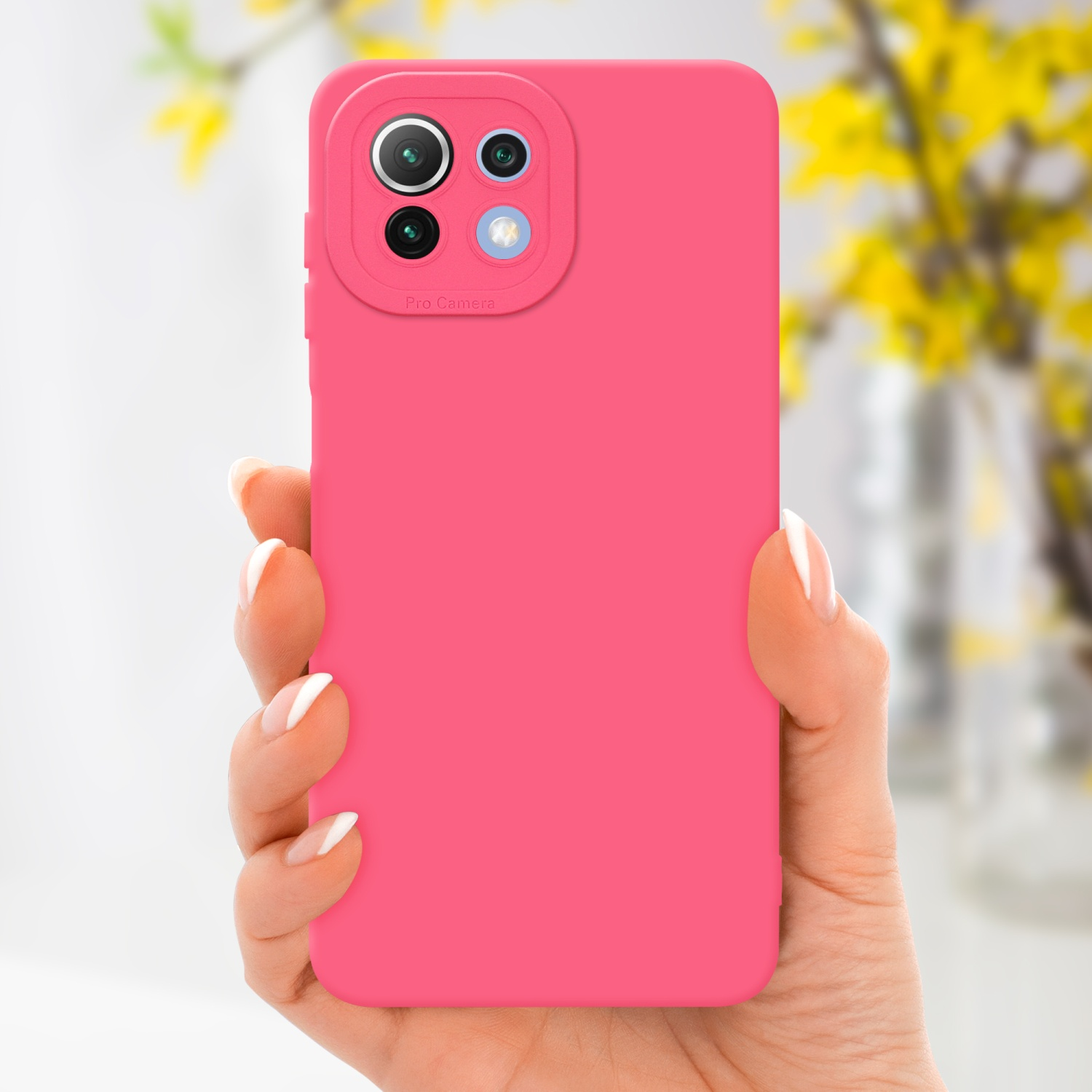 Main tenant une coque rose, fleurs jaunes en arrière-plan.