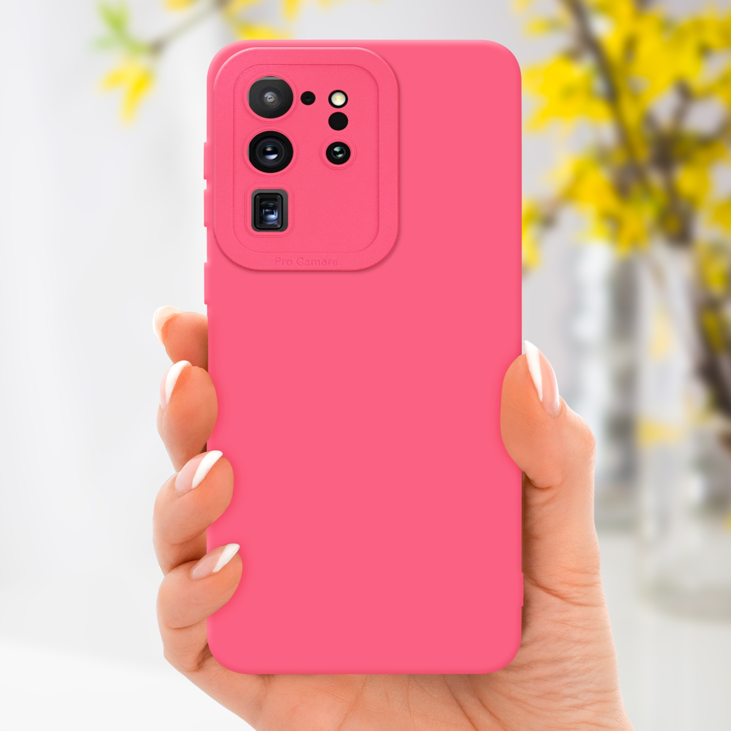 Una mano tiene un telefono rosa. Il telefono ha un modulo fotocamera. Un fiore giallo sullo sfondo sfocato.