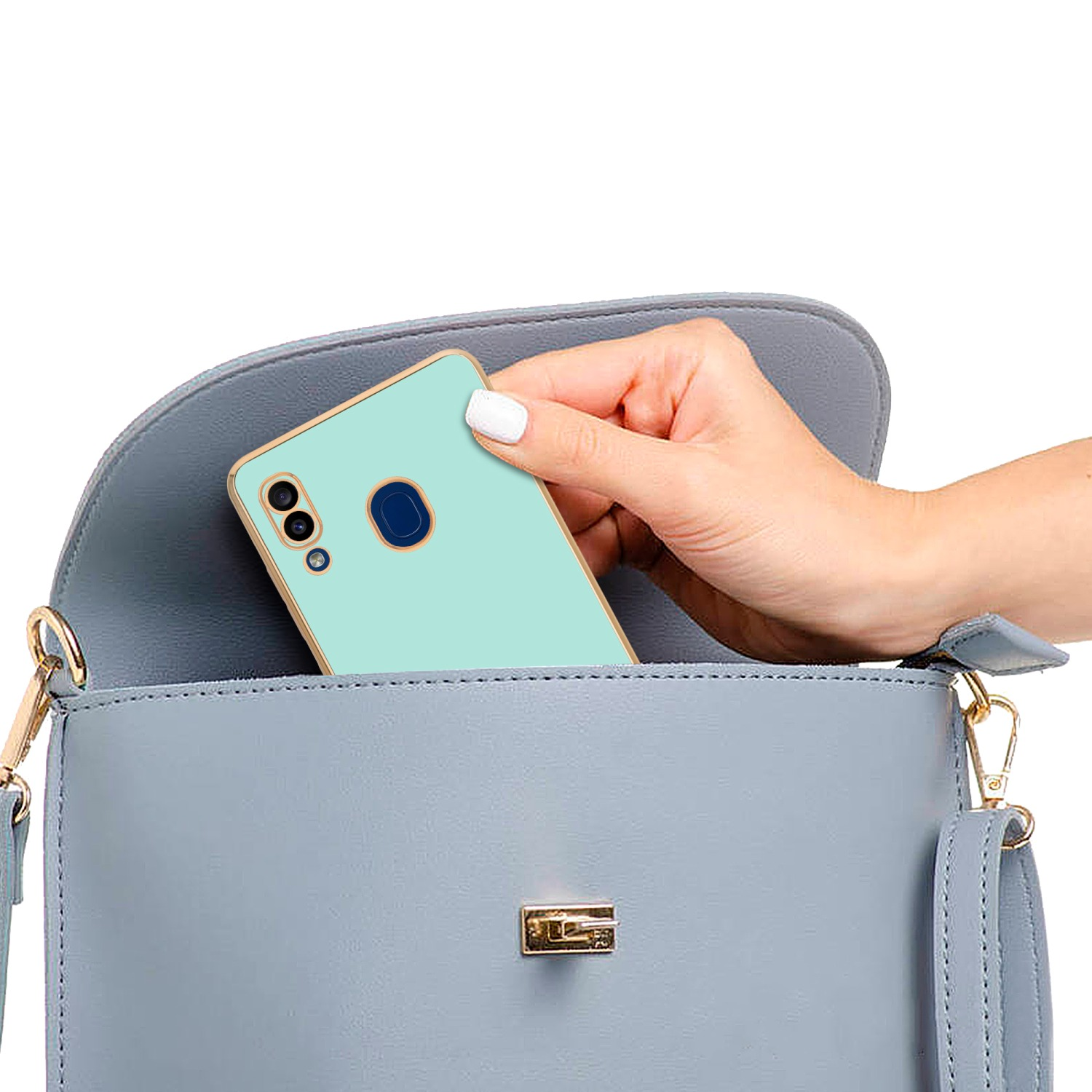 Hand legt mintgrünes Telefon in blaue Handtasche, goldene Akzente sichtbar.