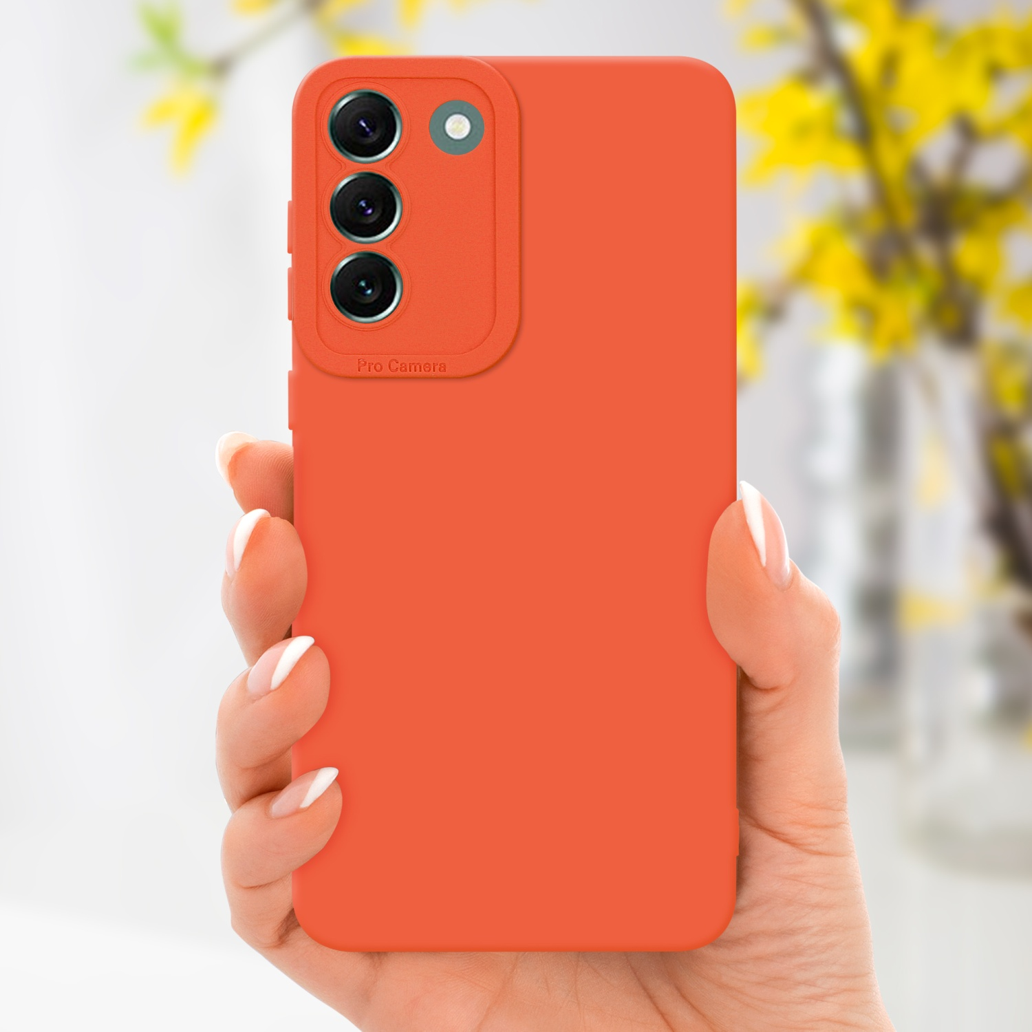 Mano che tiene una custodia per telefono arancione con tre fotocamere. Fiori sfocati sullo sfondo.