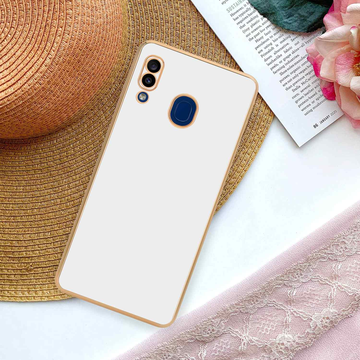 Ein weißes Telefon mit Goldrand liegt auf einem Strohhut und einem rosa Tuch.