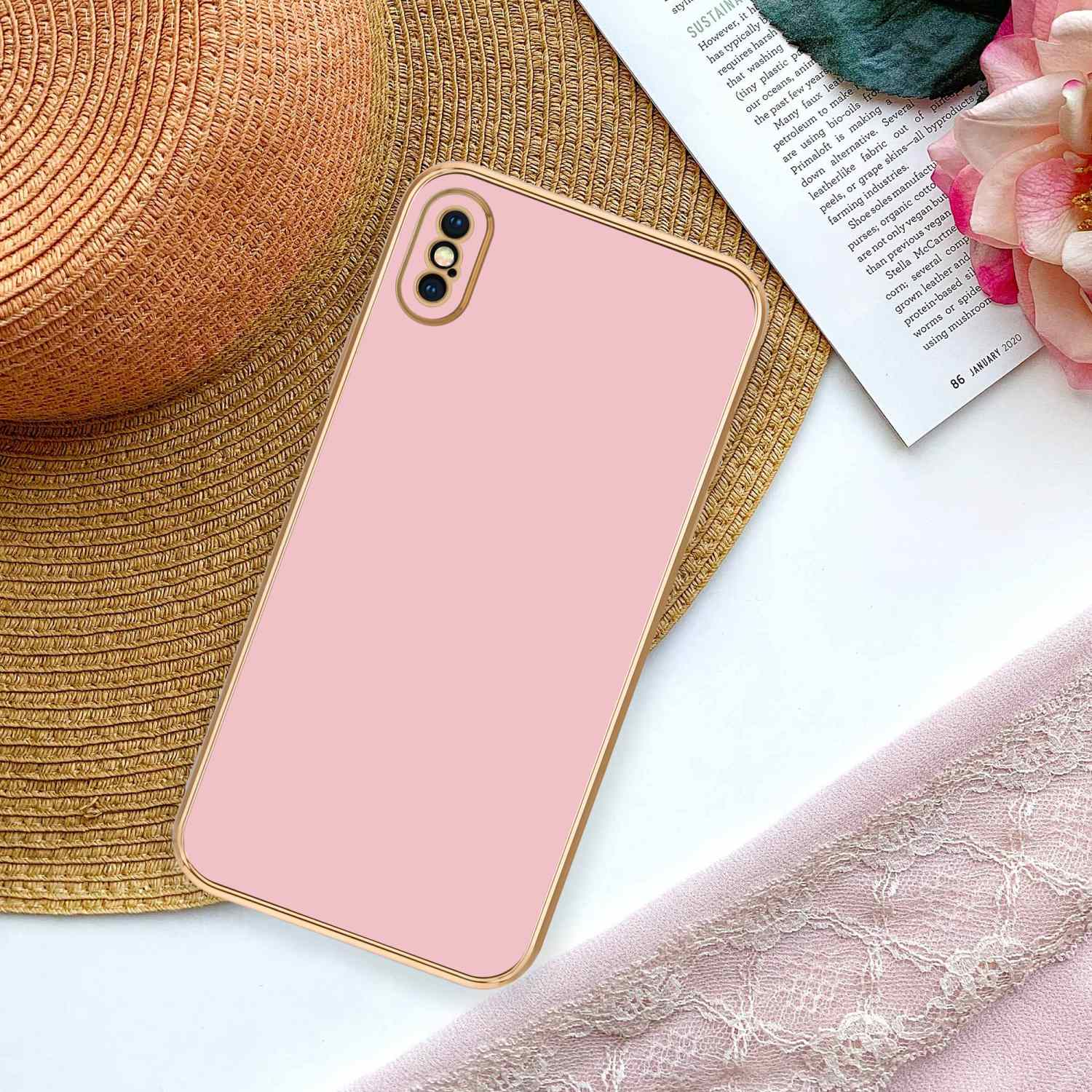 Eine rosa Handyhülle mit goldenen Rändern auf einem Hut. Ein Magazin und rosa Stoff sind im Hintergrund.