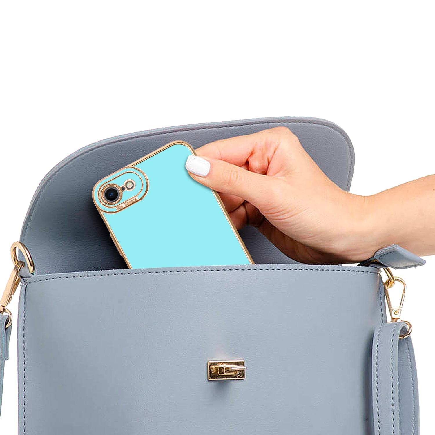 Eine Hand legt ein hellblaues Telefon in eine graue Handtasche. Goldakzente sichtbar.