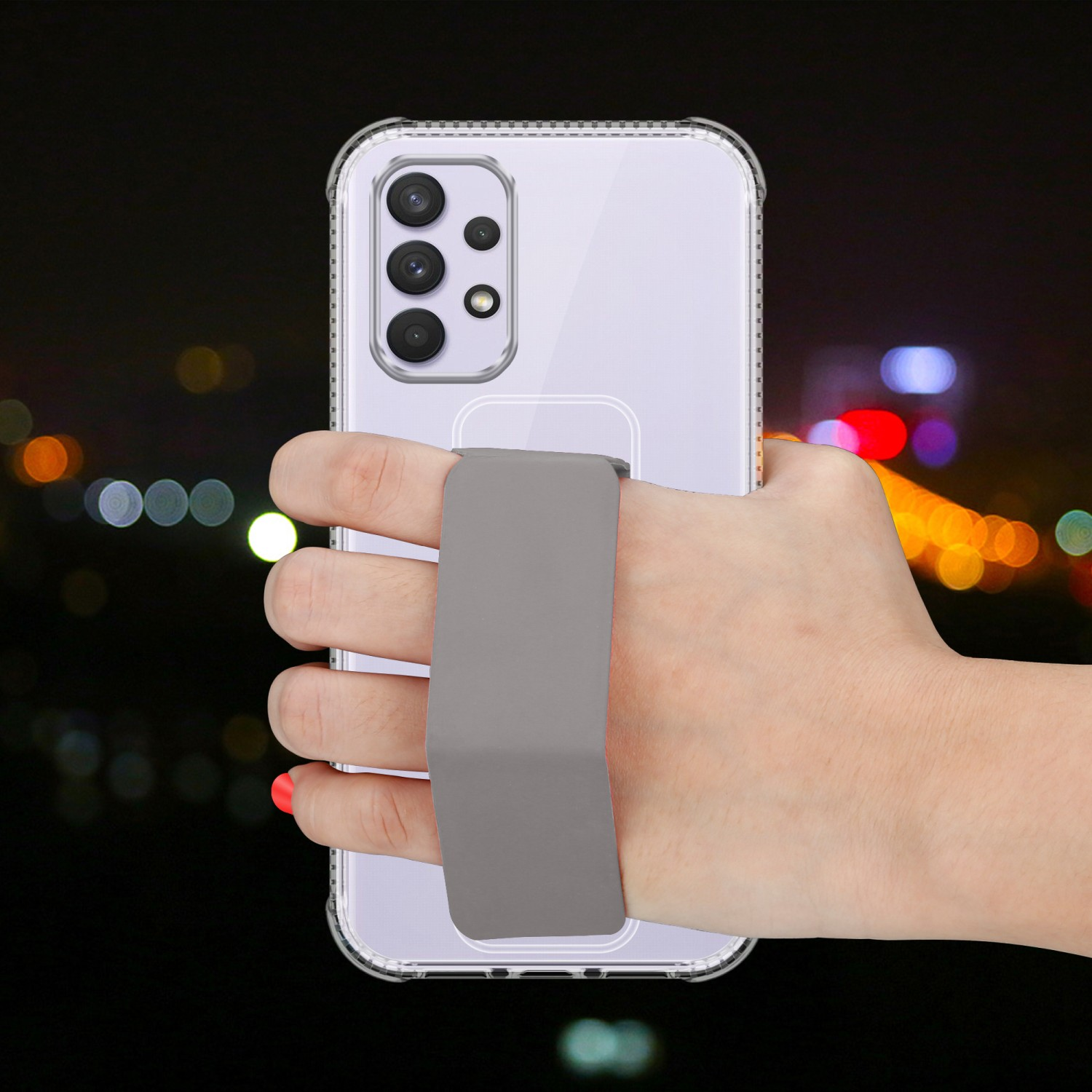 Eine Hand hält ein Telefon mit einer transparenten Hülle und einem grauen Riemen. Der Hintergrund ist eine verschwommene Nachtszene.