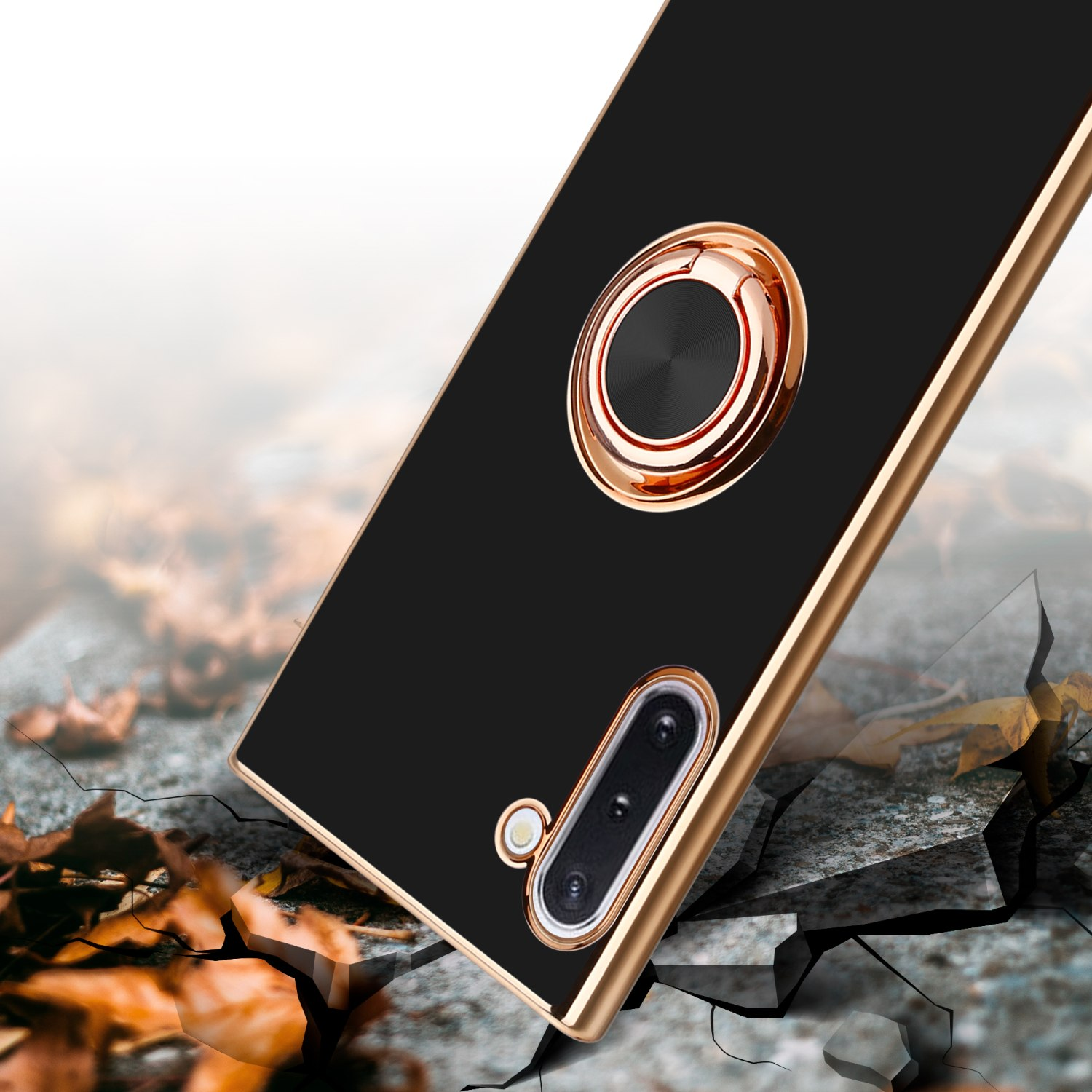 Custodia per telefono nera con anello dorato, posta su una superficie incrinata, con sfondo sfocato.