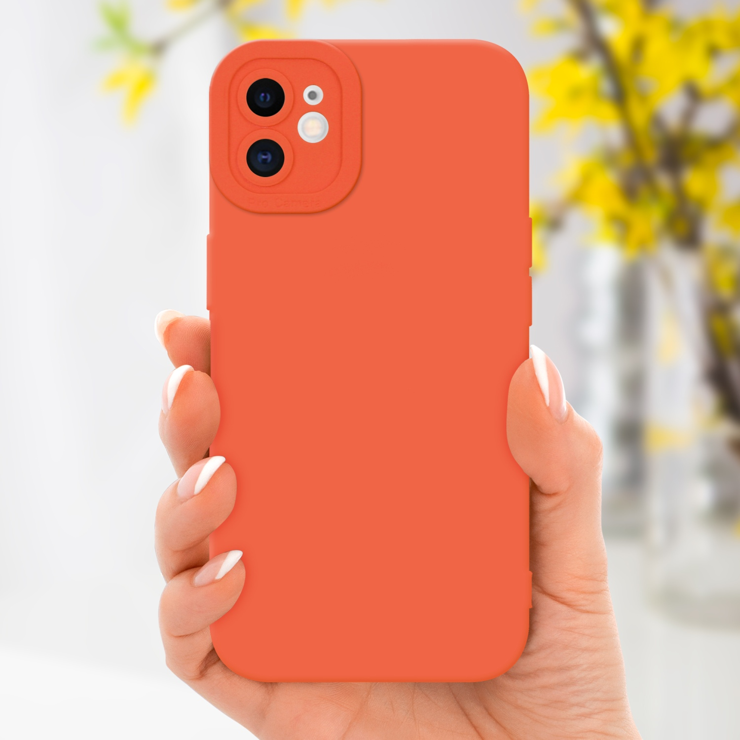 Una mano che tiene una custodia arancione per telefono, con uno sfondo sfocato di fiori gialli.