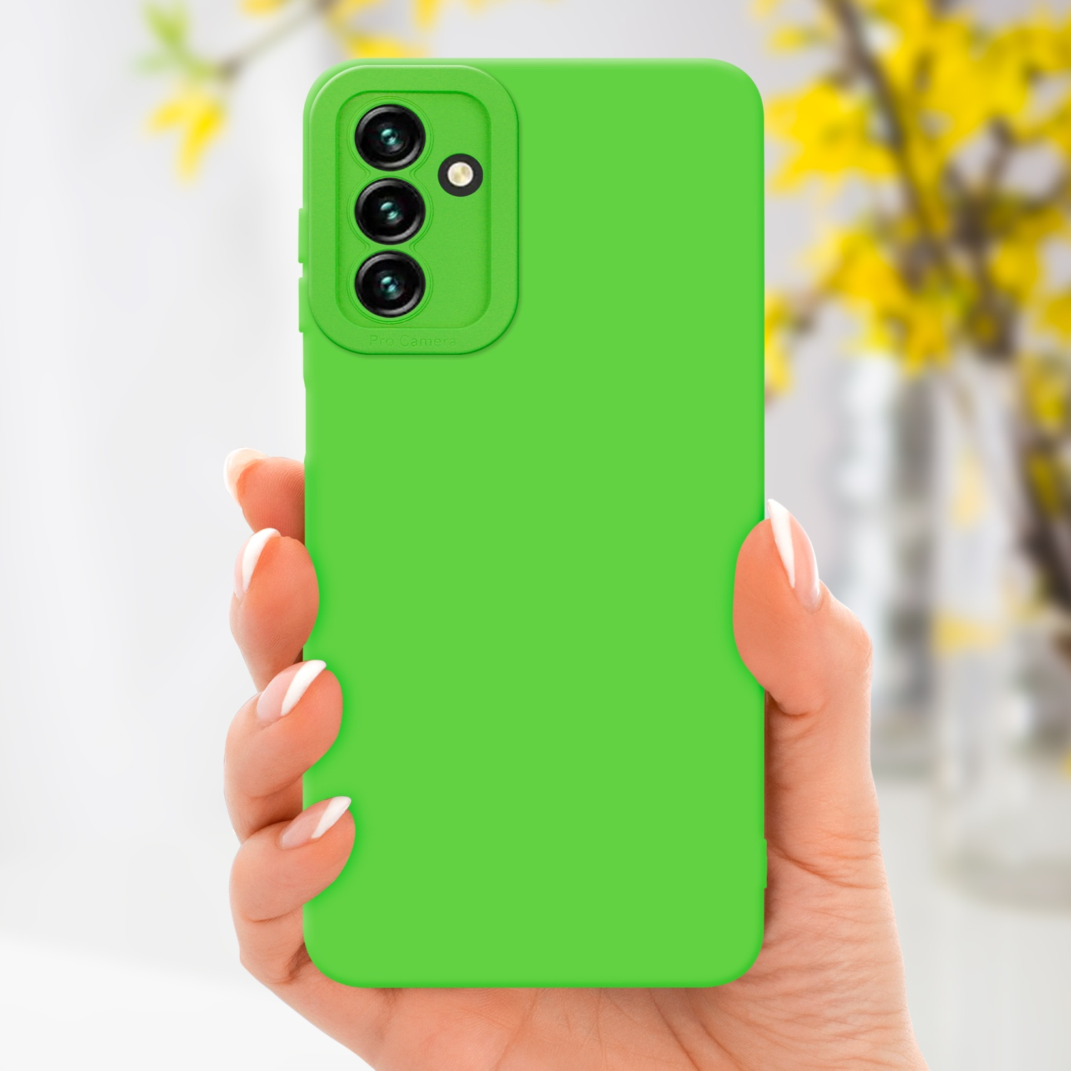 Mano che tiene un telefono verde con sporgenza della fotocamera. Fiori gialli sfocati sullo sfondo.