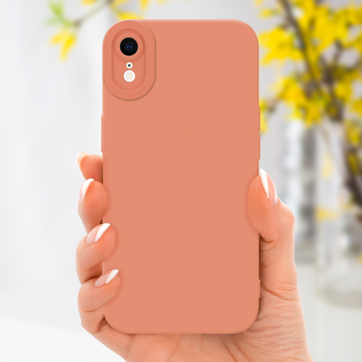 Mano che tiene una custodia per telefono arancione con una fotocamera. Fiori sfocati sullo sfondo.