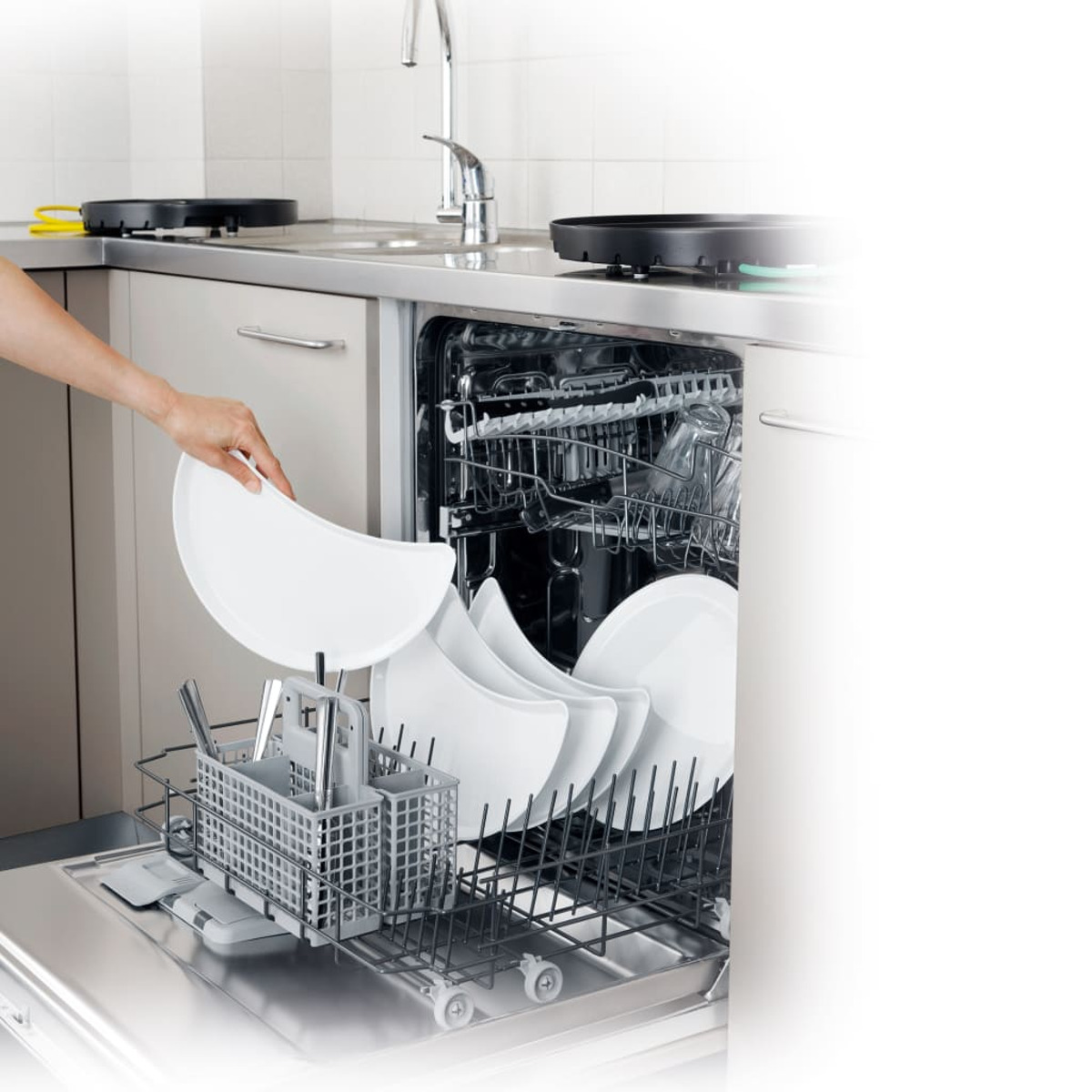 Osoba wkłada białe talerze do zmywarki. Inne naczynia są w środku.