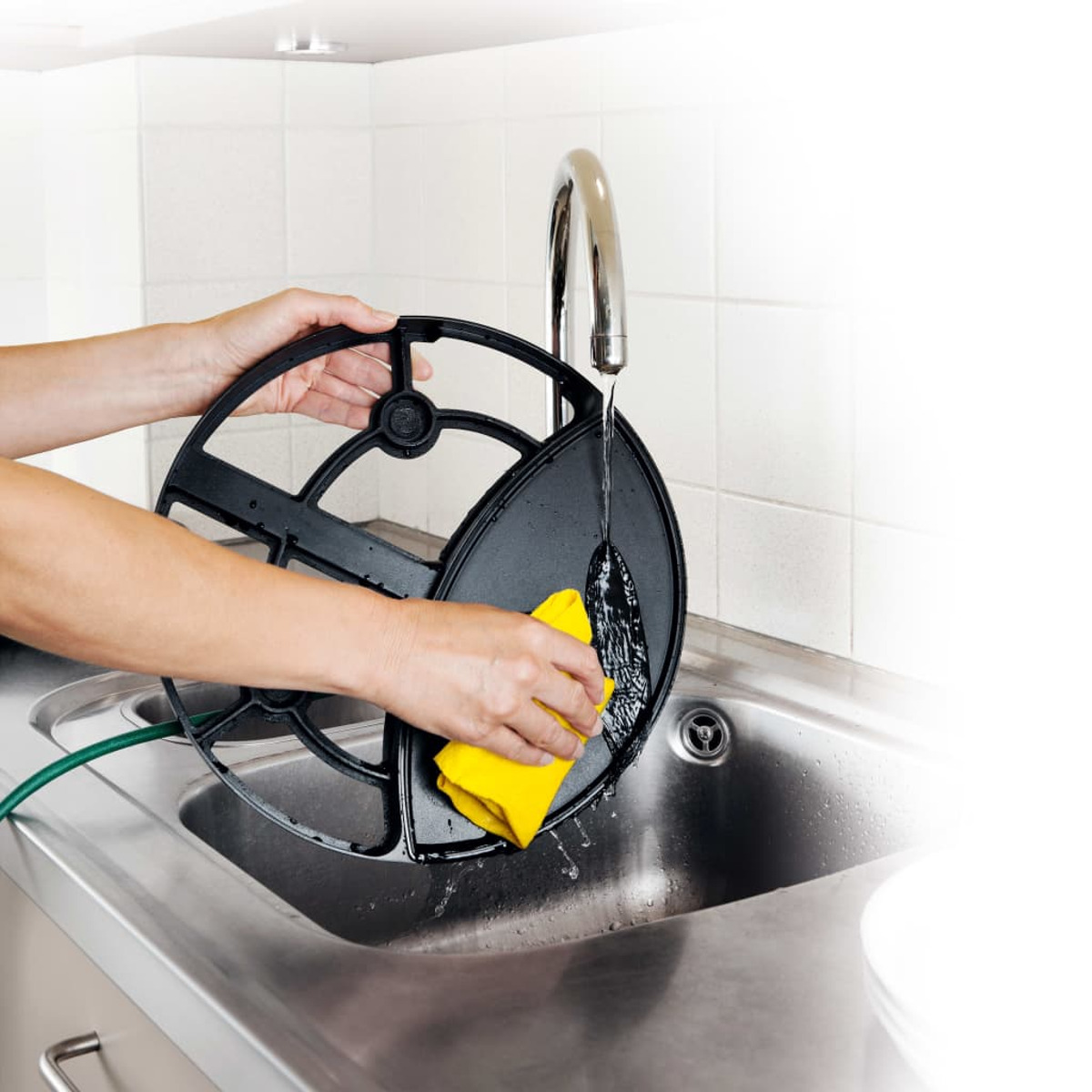 Ręce myjące czarny filtr pod srebrnym zlewem żółtą szmatką. Białe tło.