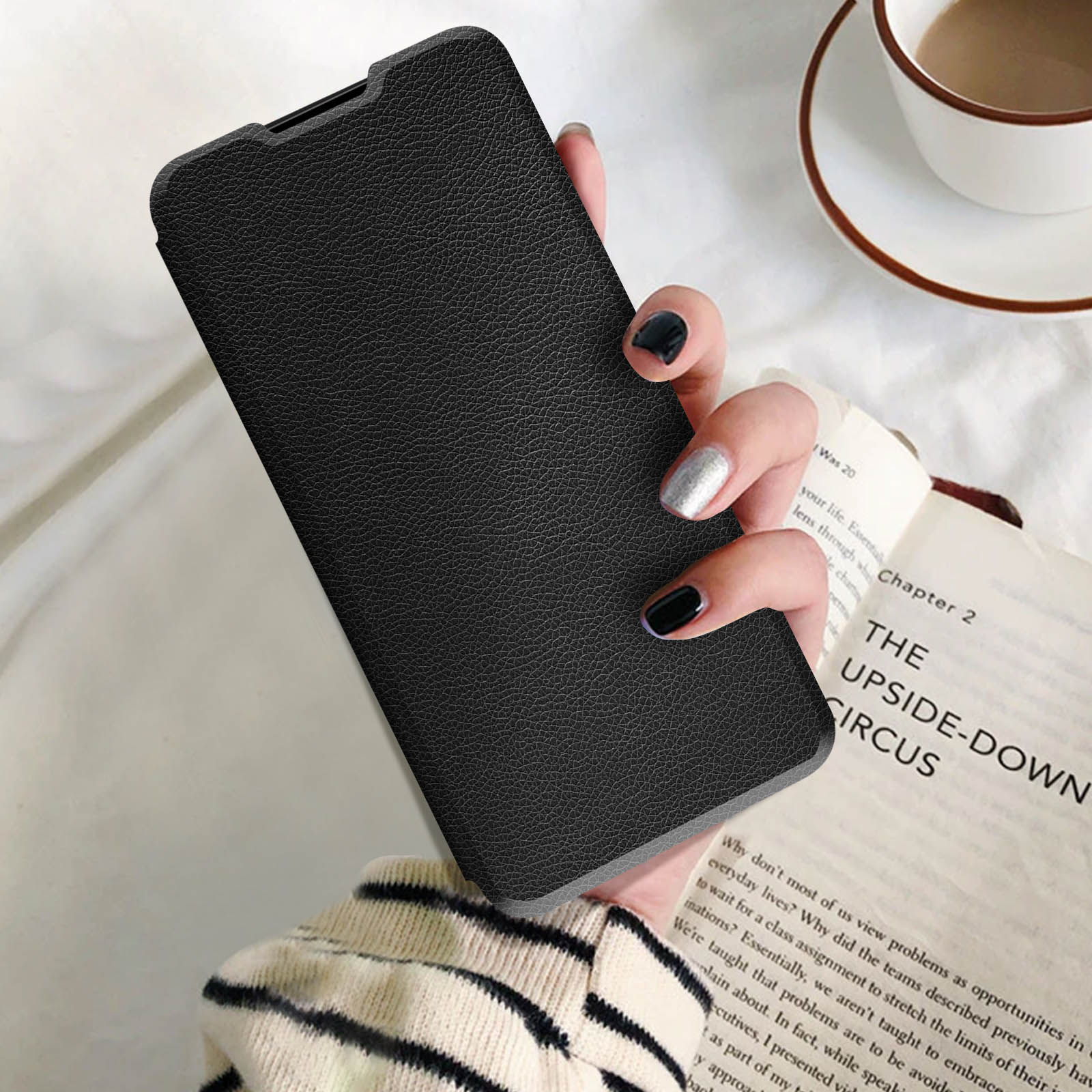 Mano che tiene una custodia nera per telefono, un libro sullo sfondo, una tazza di caffè è visibile.