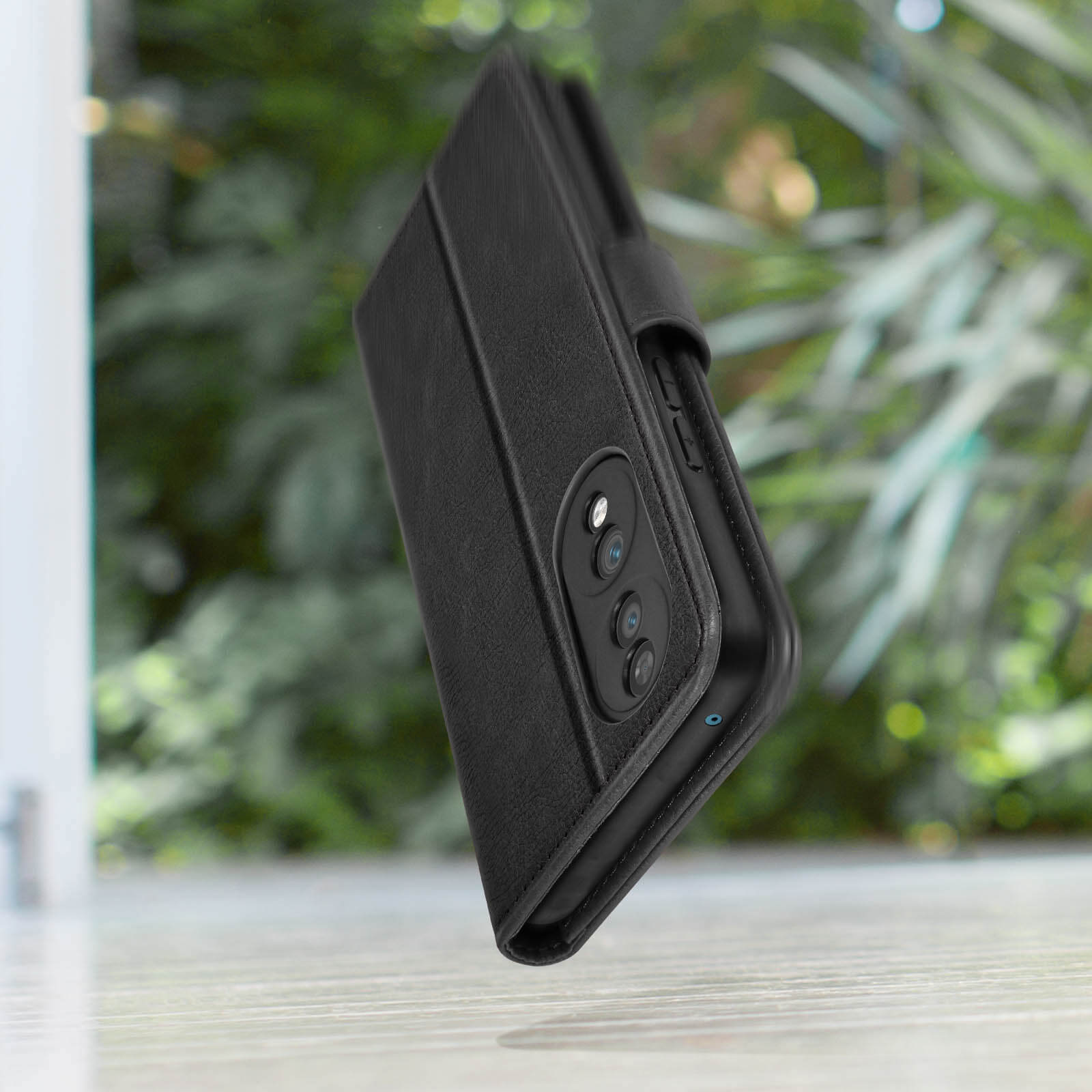 Custodia nera con telefono dentro, parzialmente aperta, su sfondo verde sfocato.