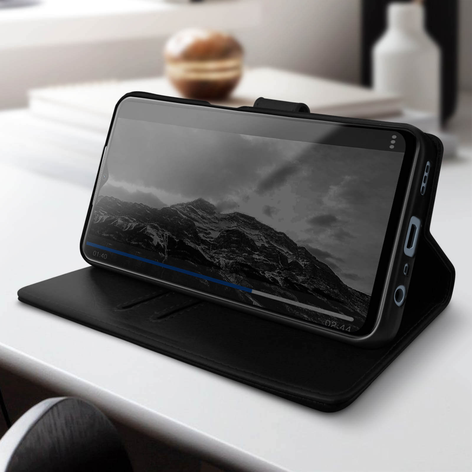 Un téléphone noir dans une coque noire, montrant une vidéo de paysage de montagne sur son écran. La coque est ouverte.
