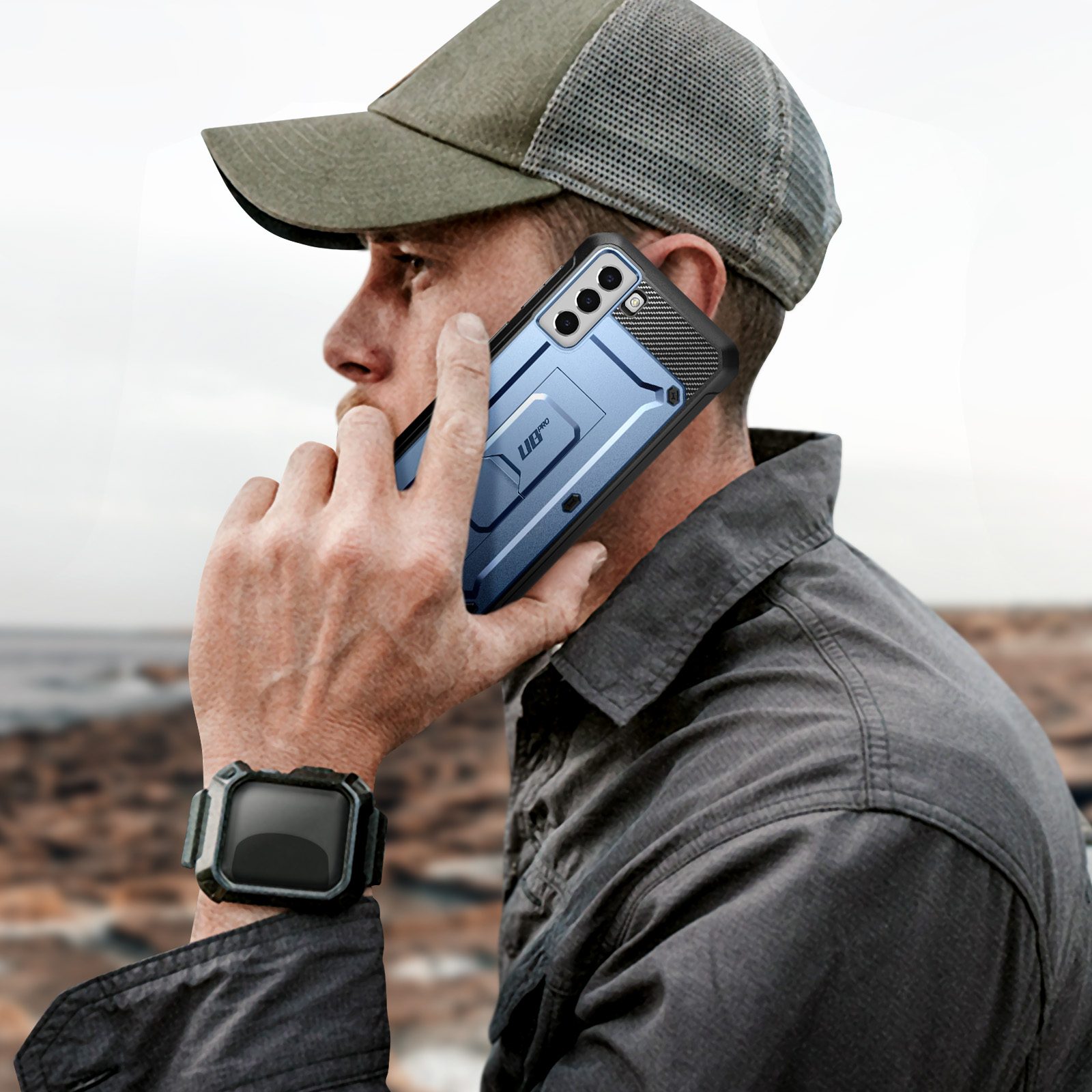Un uomo che tiene un telefono blu. Indossa un cappello e uno smartwatch.