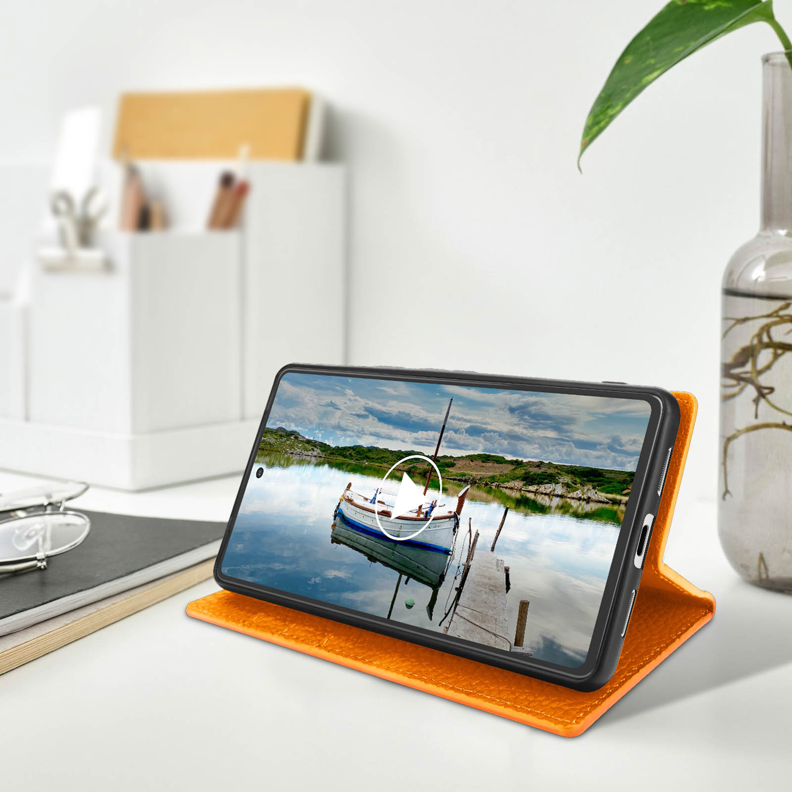 Un téléphone dans un étui avec un écran affichant une scène de lac. Un étui orange est ouvert sur une table.