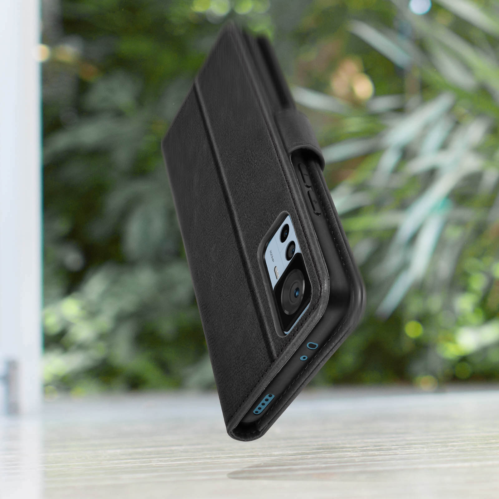 Ein schwarzes Telefon in einer Hülle. Die Hülle ist offen. Der Hintergrund ist mit Blättern verschwommen.