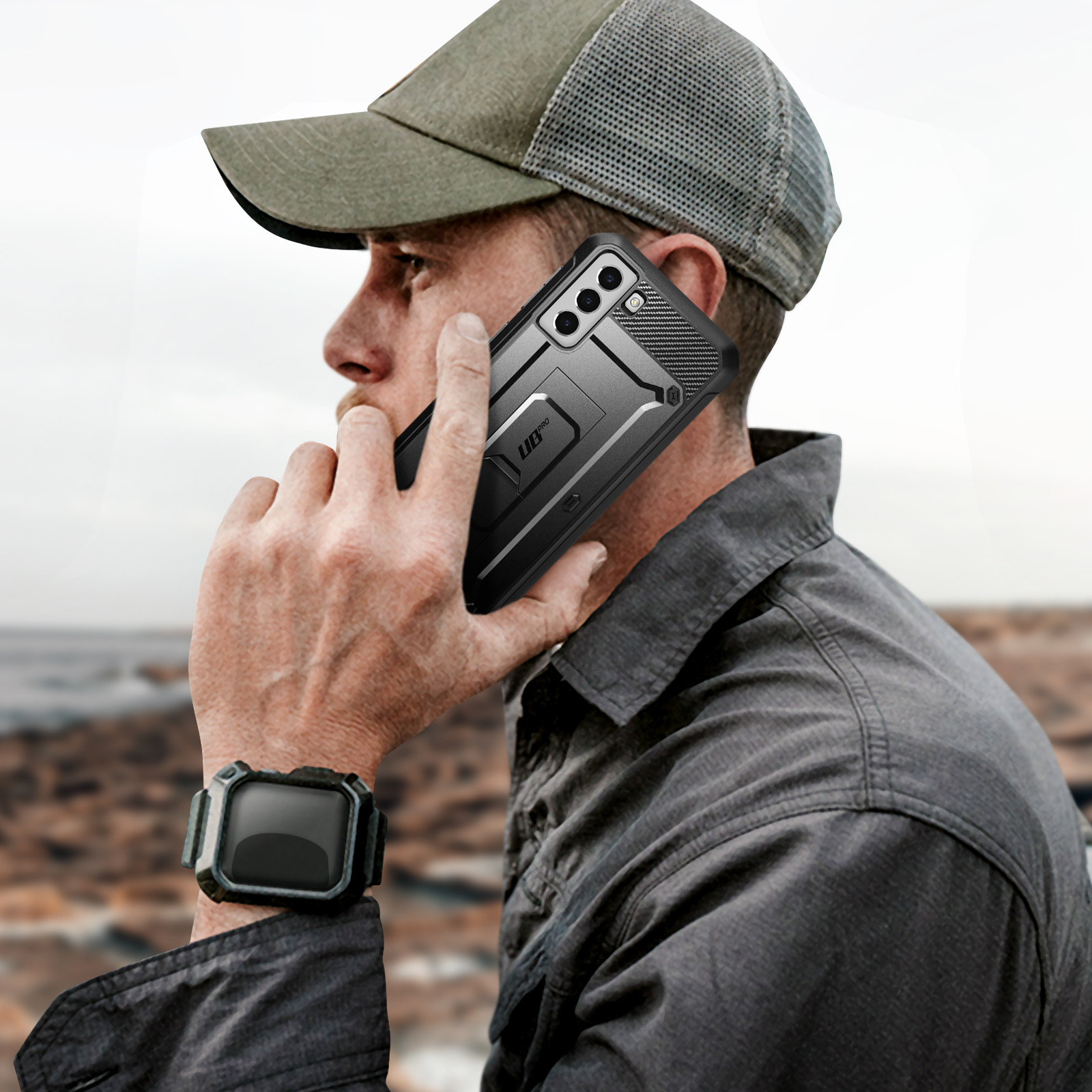 Uomo con cappello, tiene un telefono nero in una custodia nera, parla al telefono.